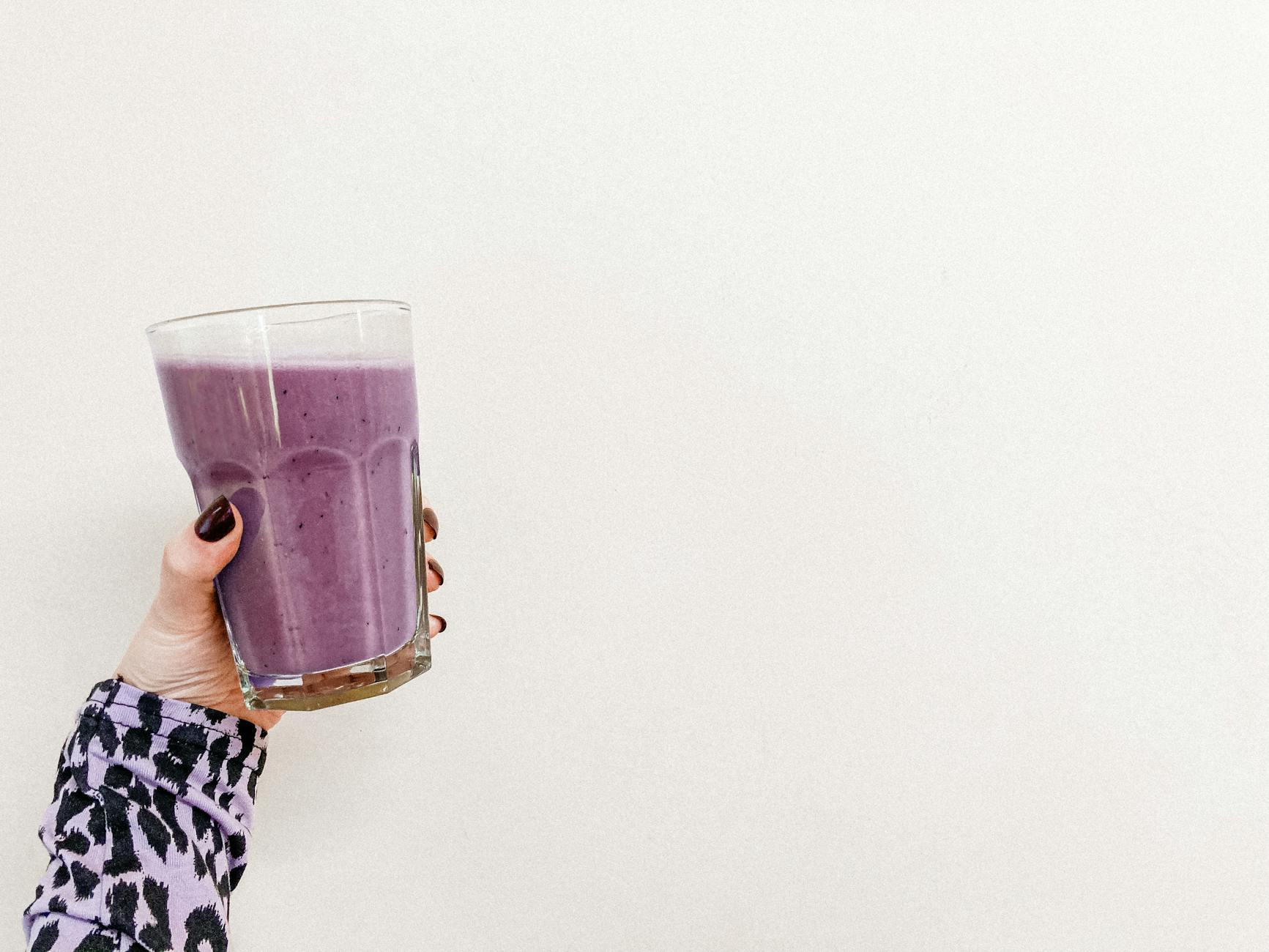 A person's hand holding a healthy purple smoothie in a glass with a white background. Perfect for health and wellness themes. - healthy smoothie recipes