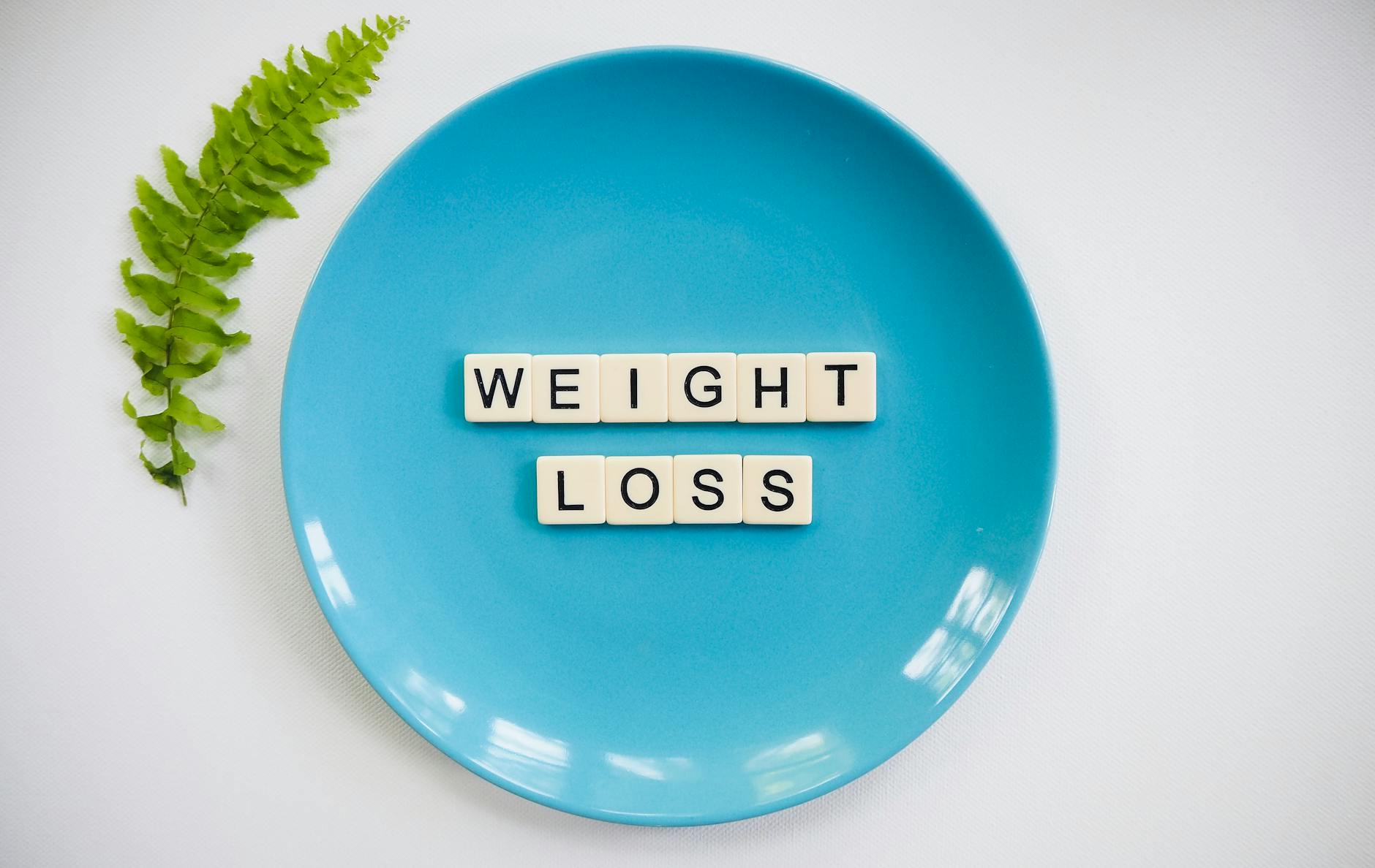 A blue plate with 'weight loss' tiles and a fern leaf on white background. - healthy weight loss