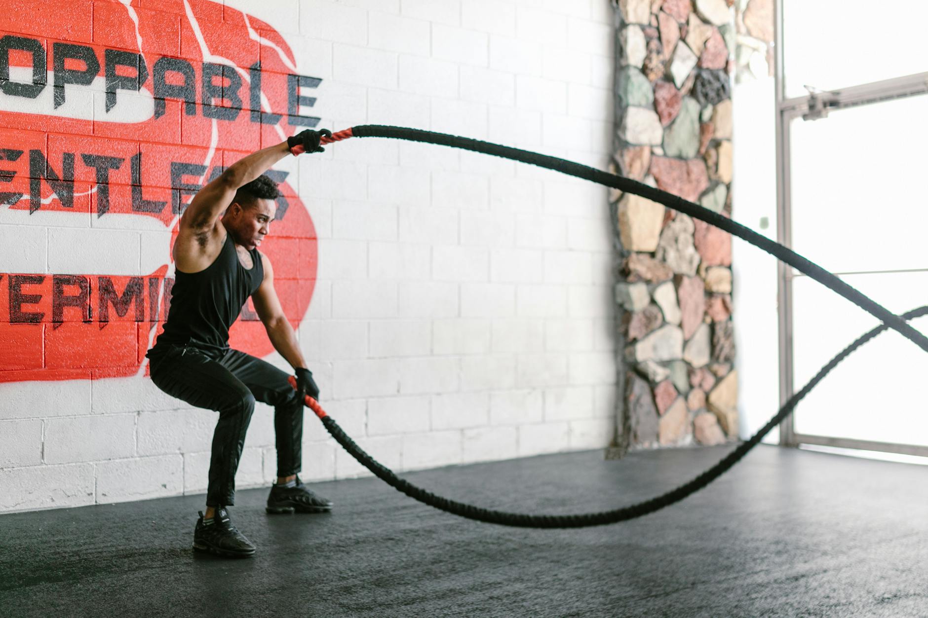 A focused man performs a dynamic battle rope workout in a modern gym setting, showcasing strength and endurance. - hiit fat burning