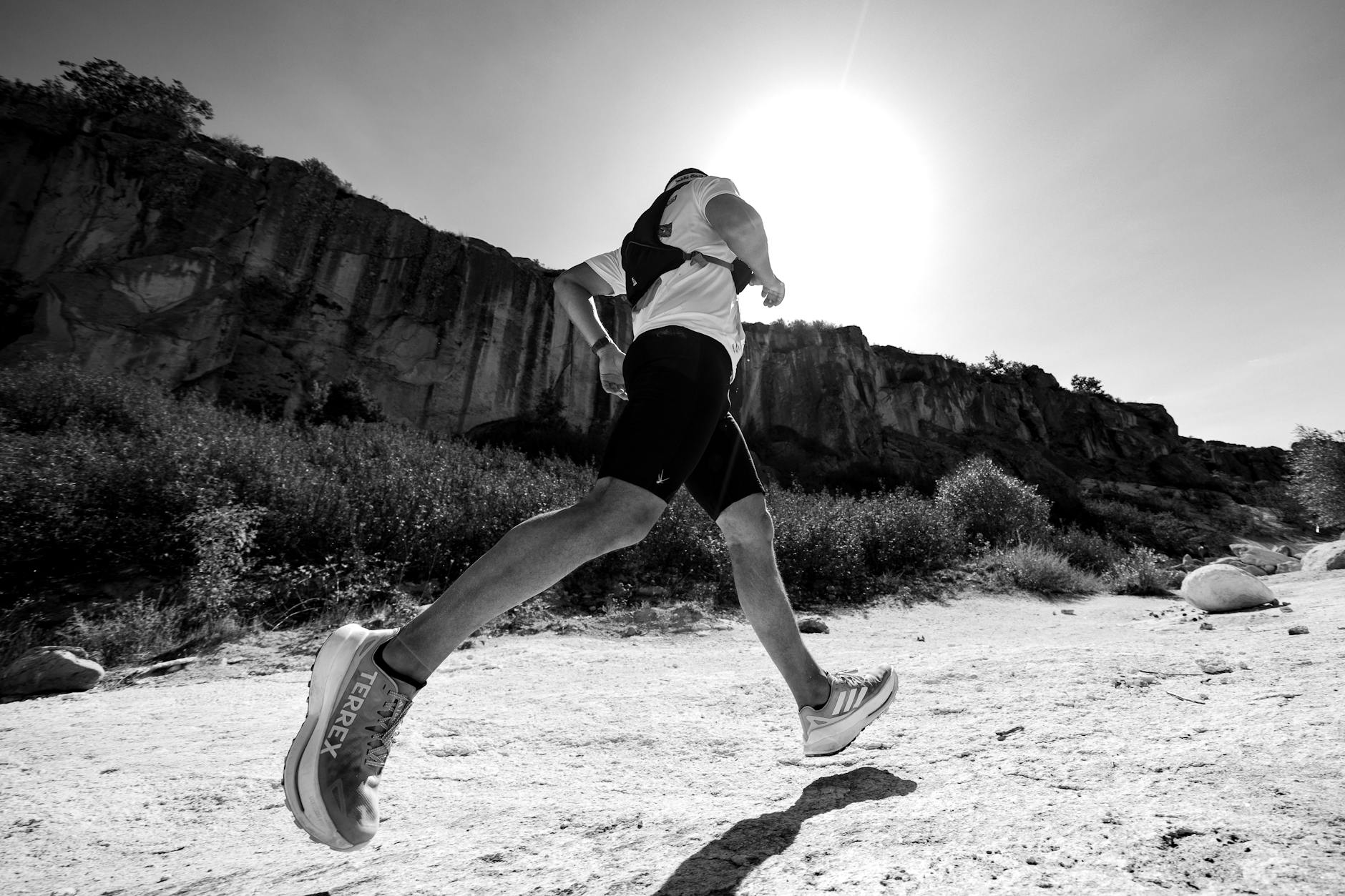 Black and white photo of a trail runner beneath a sunny cliff, showcasing movement and determination. - hiking endurance training