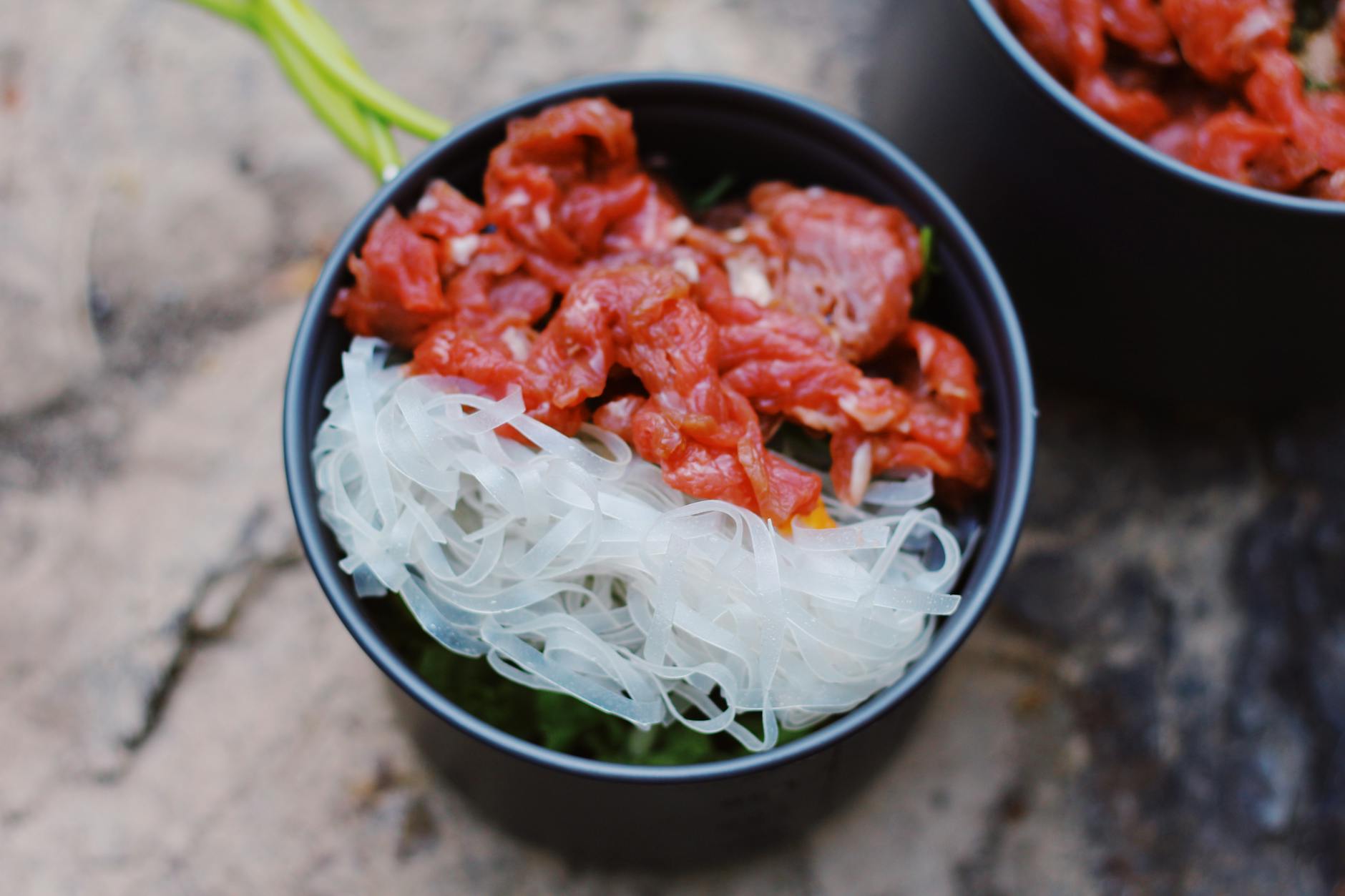 From above of bowl with rice noodles and red raw meat placed on blurred background - hiking nutrition tips