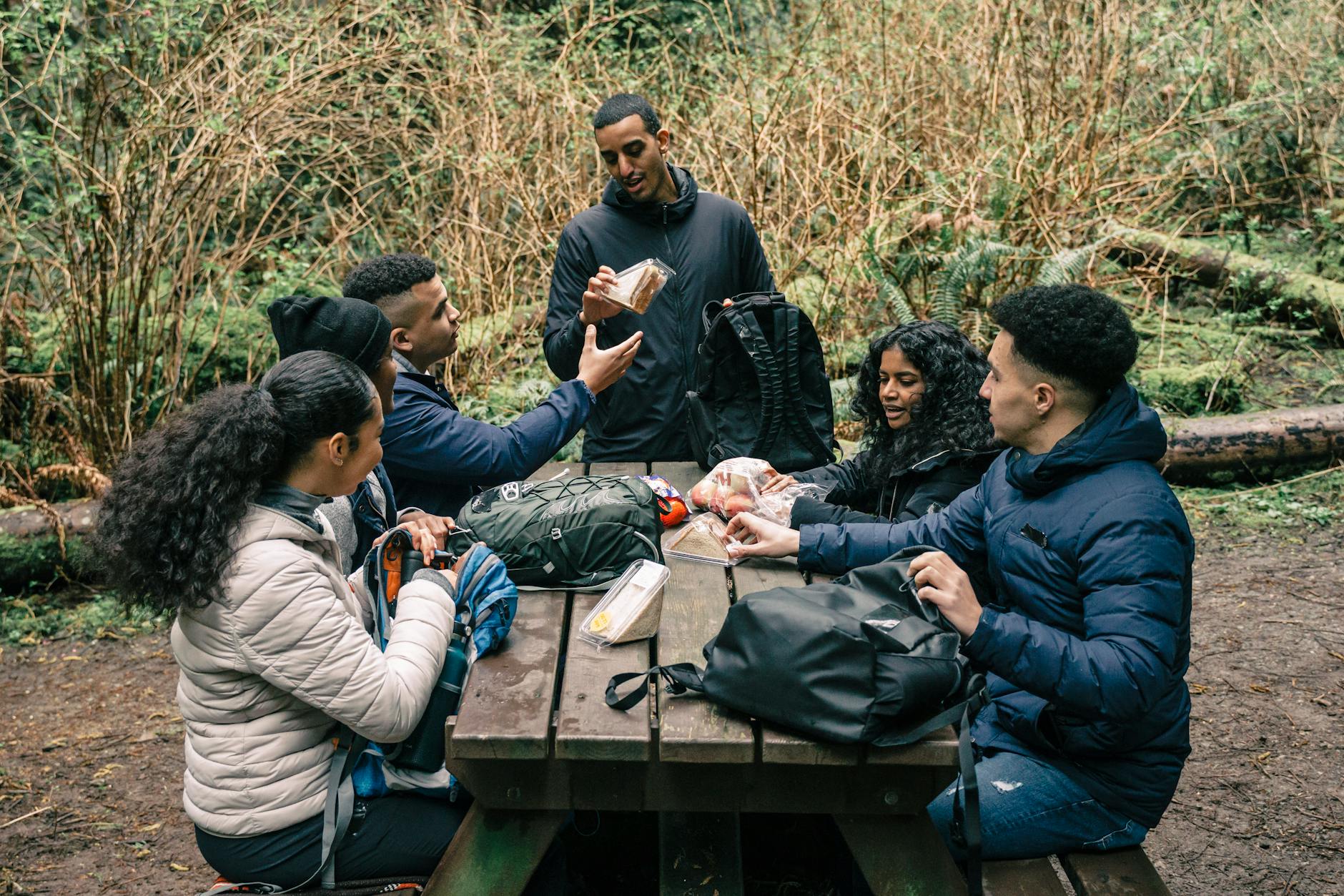 A diverse group of friends sharing snacks at a picnic table in a forest setting during a hiking trip. - hiking nutrition tips