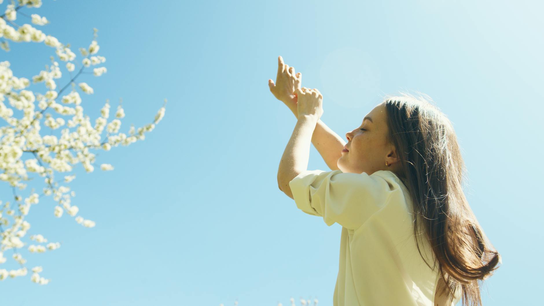 A serene moment with a young woman raising her hands under the clear blue sky filled with blossoming branches. - hormone balance spring