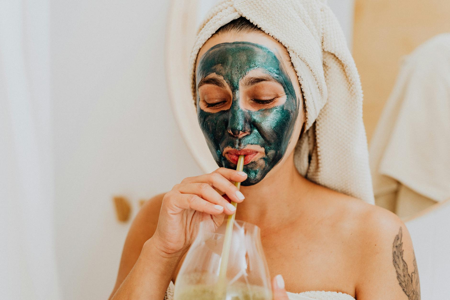 Woman enjoying a skincare routine with a face mask and a refreshing drink indoors. - hydrating recipes clear skin