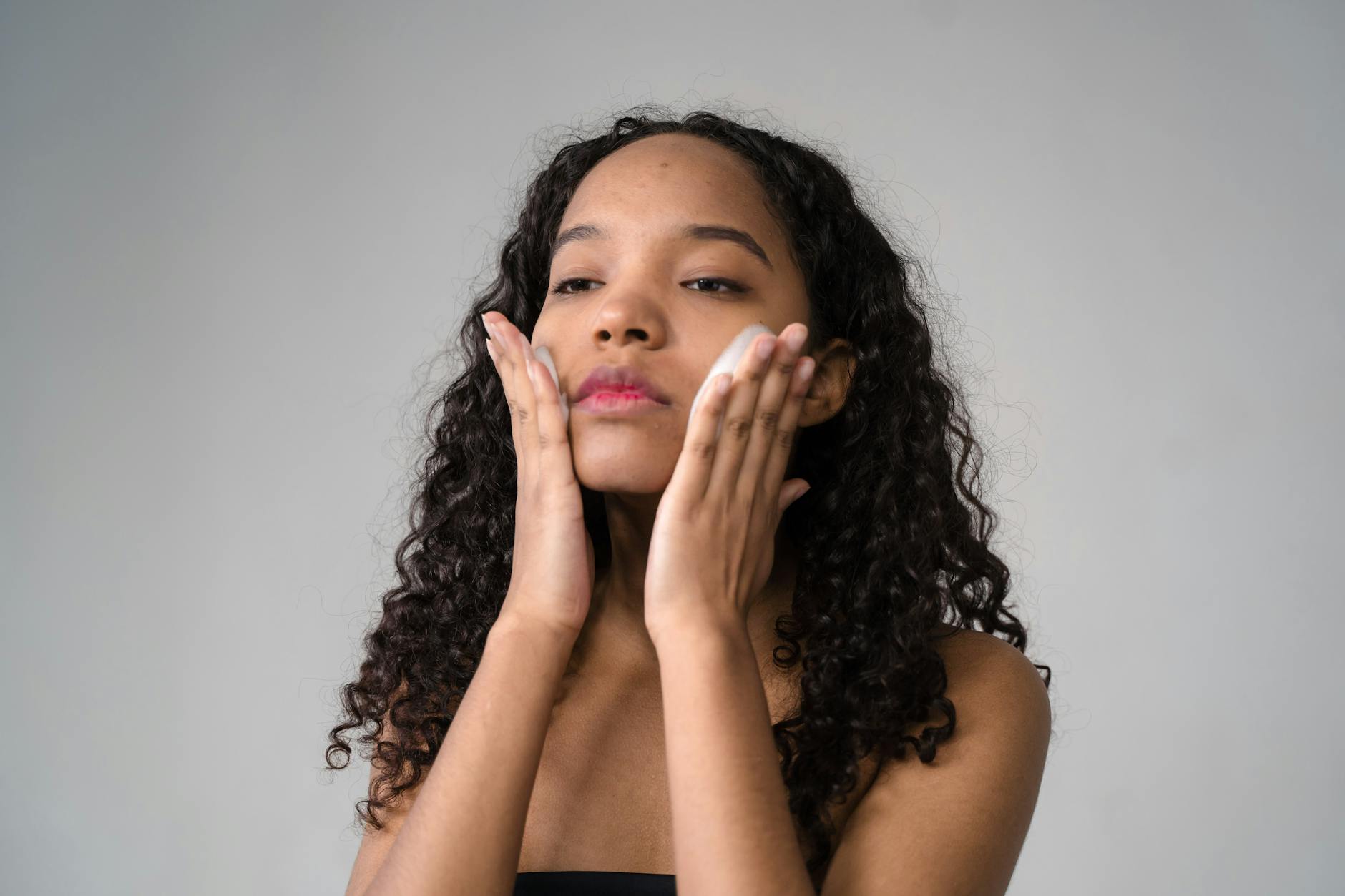 A young woman with curly hair gently applies skincare cream to her face. - hydrating recipes clear skin