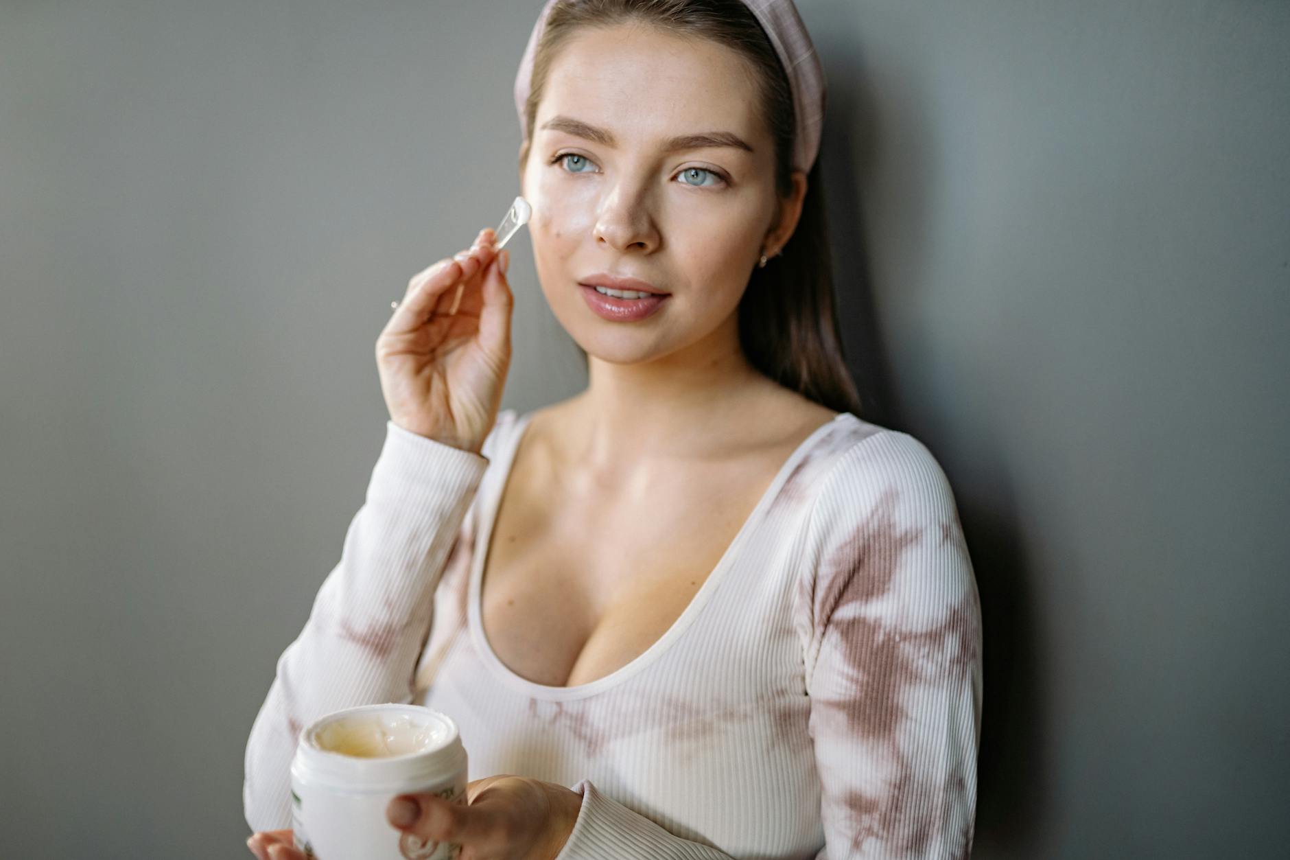 A woman in a headband applies skincare cream indoors, focusing on facial care and beauty routines. - hydrating recipes clear skin