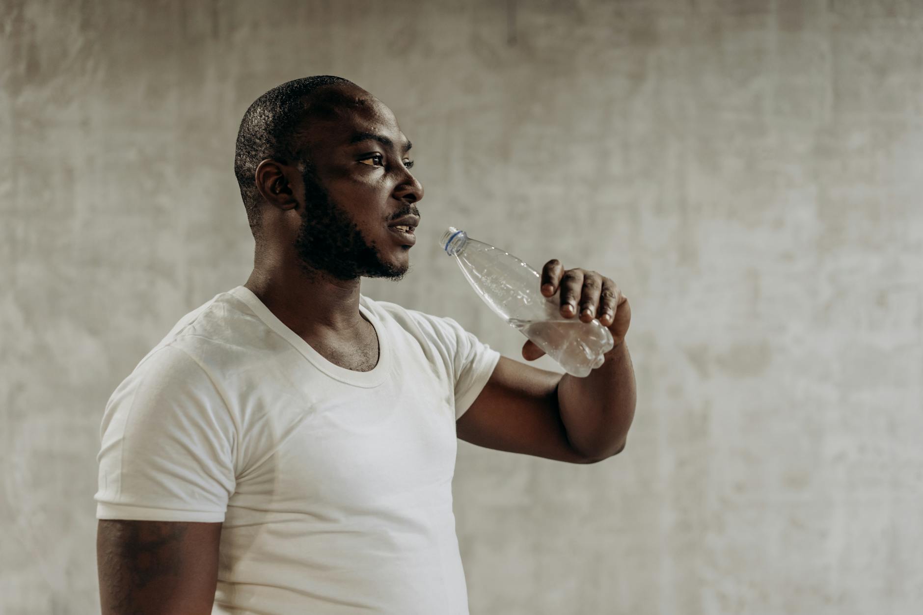 Man in white shirt drinking water after exercising indoors, promoting fitness and healthy living. - hydration for workouts