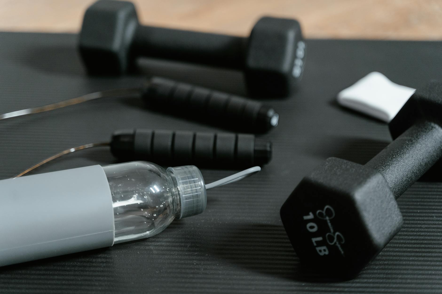 Close-up of gym essentials: dumbbells, jump rope, and water bottle on a mat. - hydration for workouts