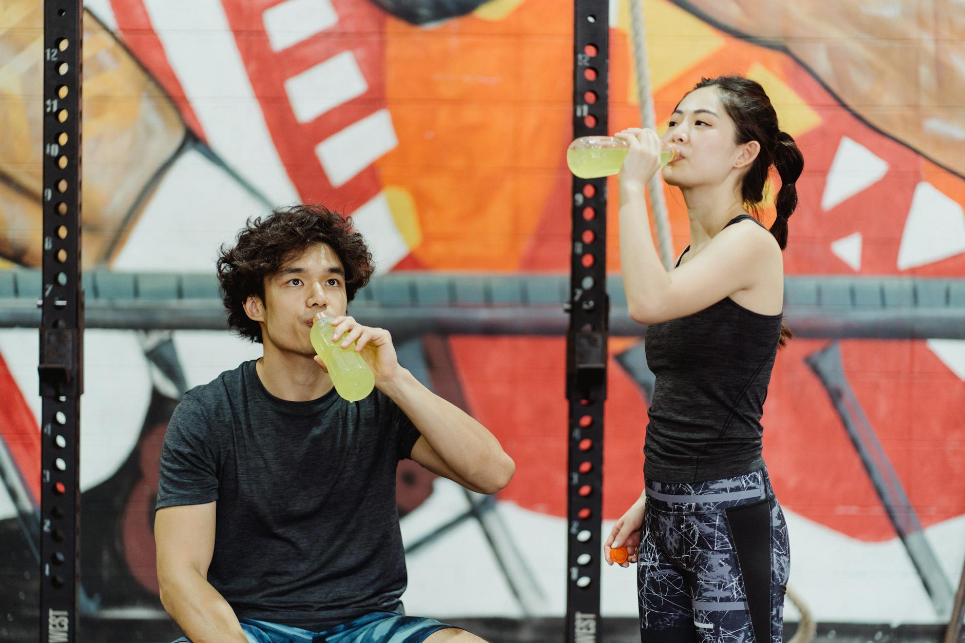 Asian couple in activewear drinking yellow beverages at an indoor gym. - hydration for workouts