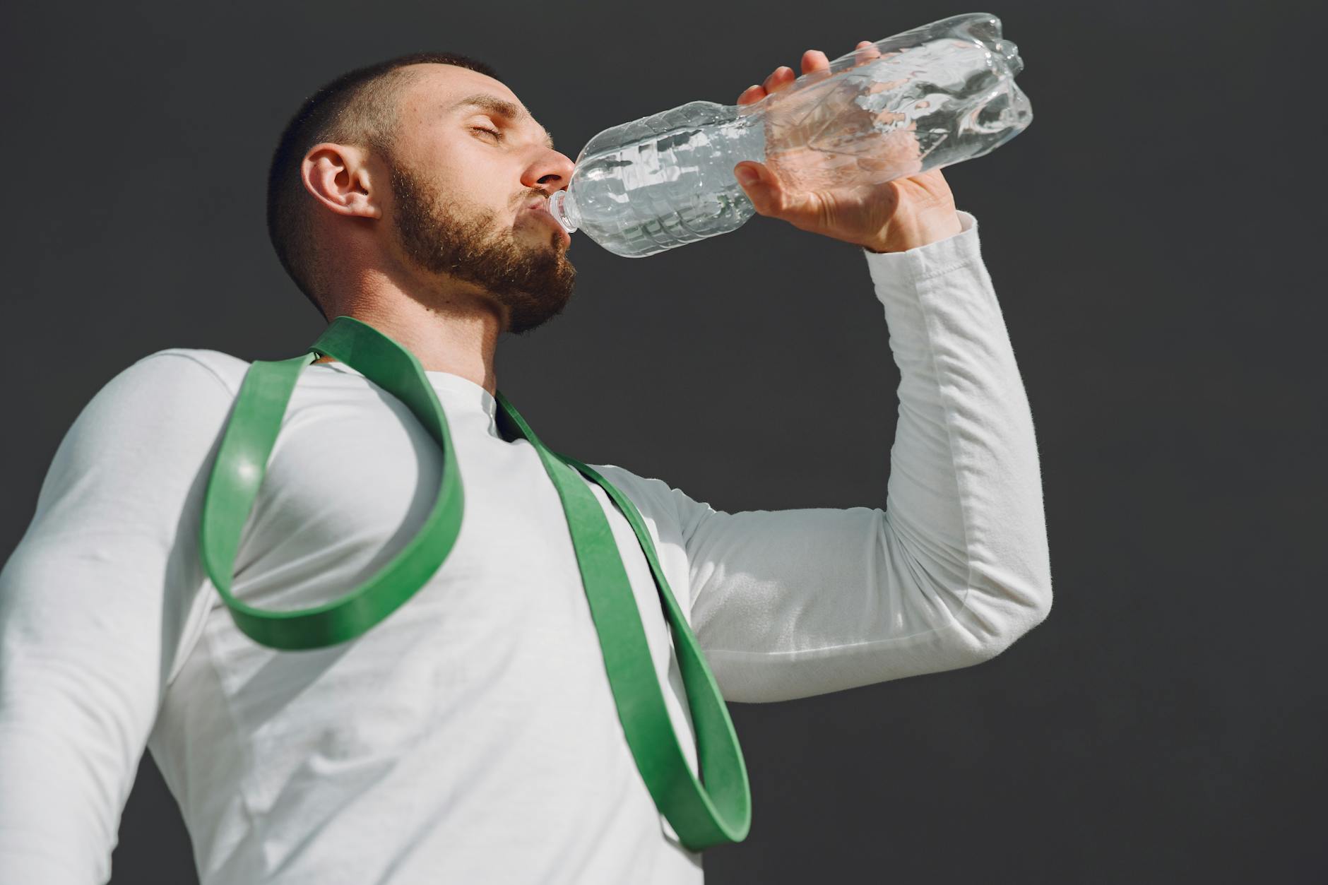 A fit man in sportswear drinking water outdoors, highlighting hydration and fitness. - hydration for workouts