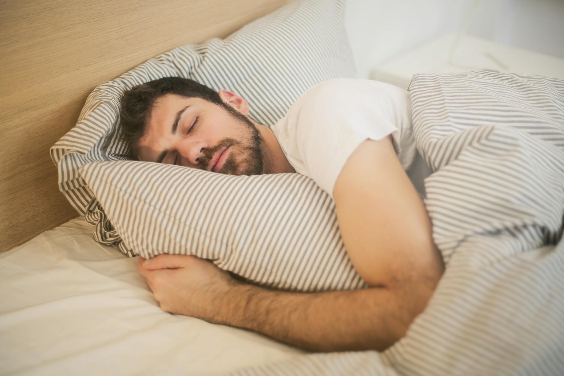 Man sleeping peacefully on striped bedding, embracing relaxation and comfort. - improve sleep quality