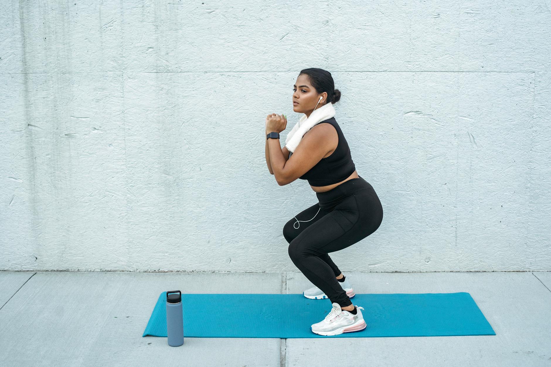 Confident woman doing squats on a yoga mat with a water bottle nearby. Fitness and lifestyle concept. - intermediate hiit workout