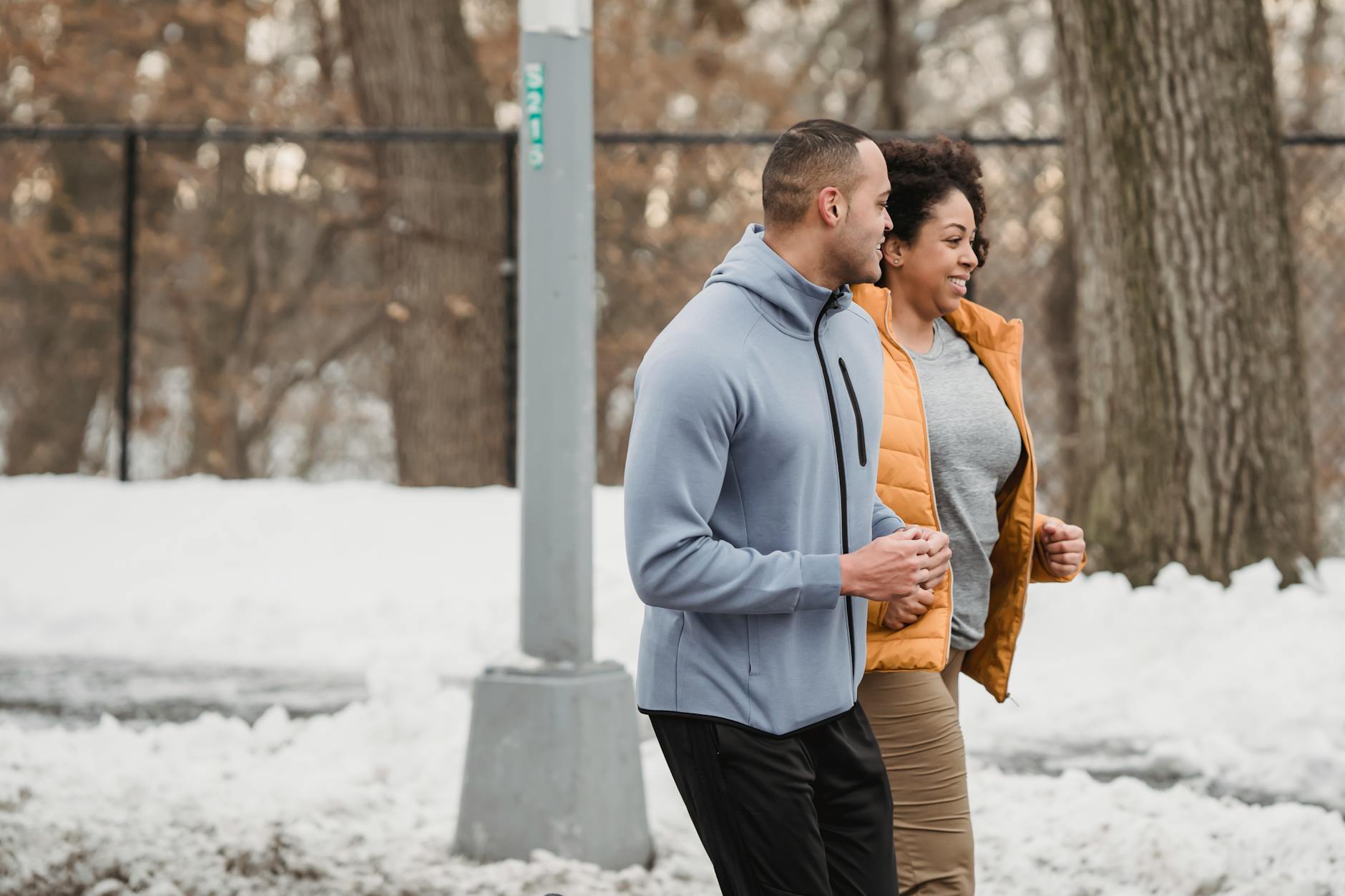 Side view smiling ethnic male trainer and plus sized black female in warm clothes running together in snowy winter park - lose winter weight