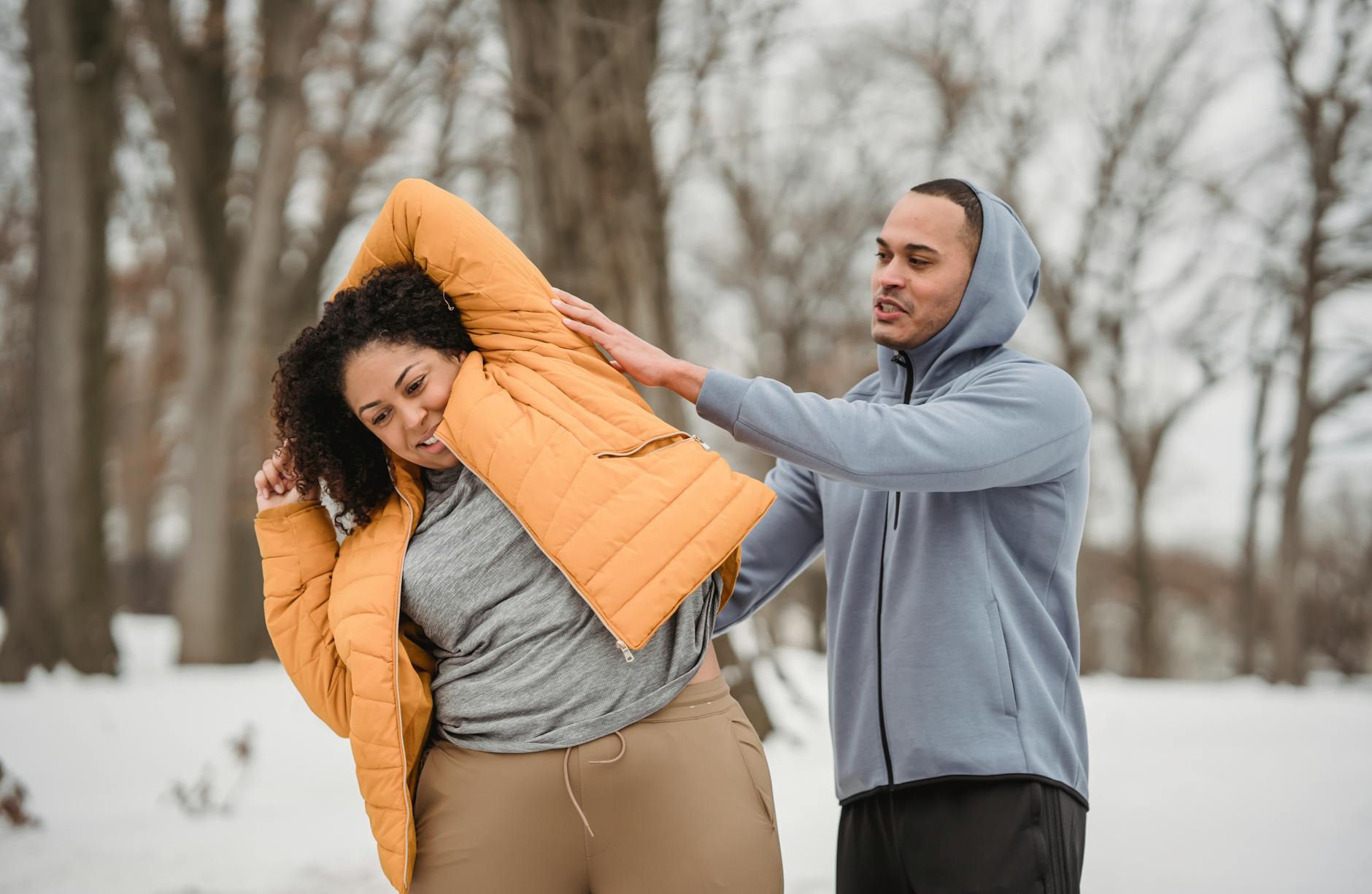 Smiling African American plus size female with hands behind head doing bend with support of personal coach in winter park - lose winter weight