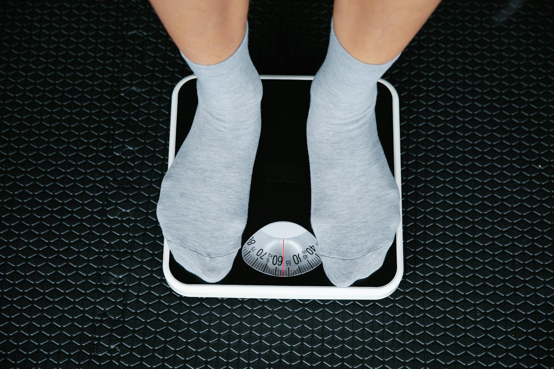 Top view of feet in socks standing on a bathroom scale, indicating weight measurement. - lose winter weight