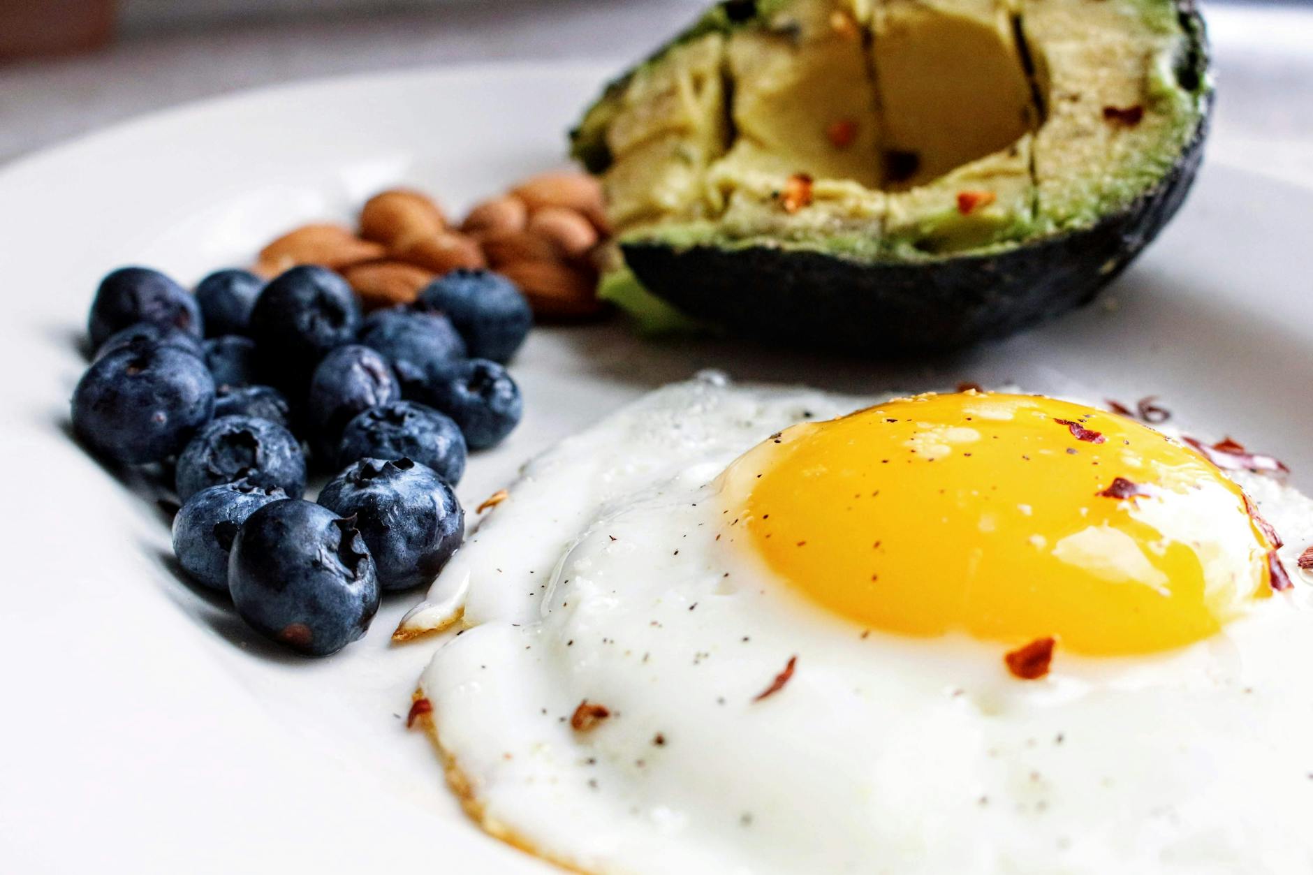A nutritious breakfast featuring a fried egg, avocado, blueberries, and almonds. - low fat low carb