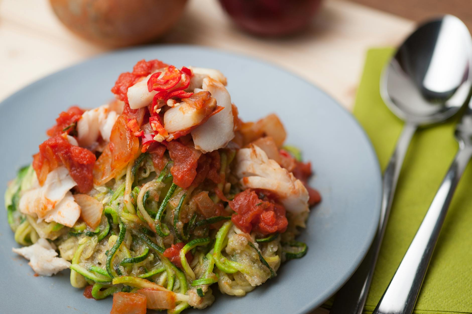 A plate of zucchini noodles topped with fresh tomato and fish, ideal for a healthy meal. - low fat low carb