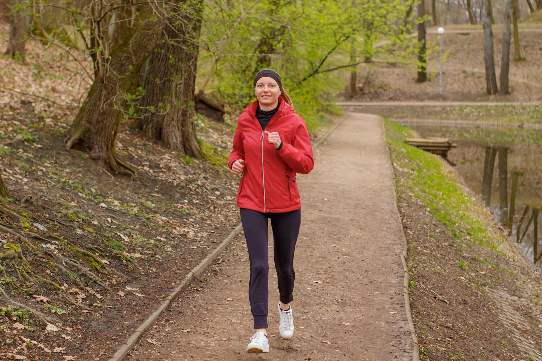 Woman in a red jacket jogging on a forest footpath during springtime. - low impact spring workouts