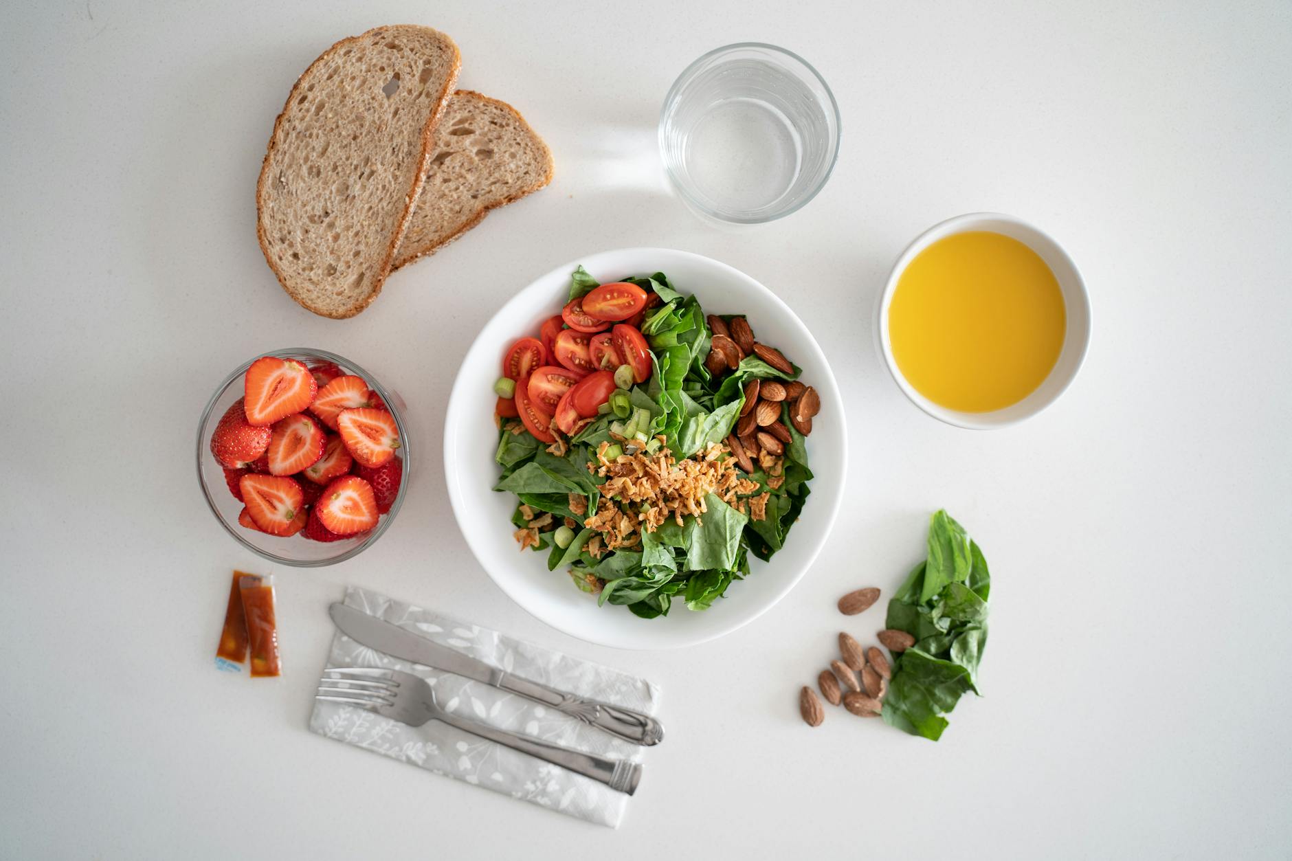 Top view of a healthy salad and fresh ingredients with bread and juice on a white surface. - macronutrient balance spring