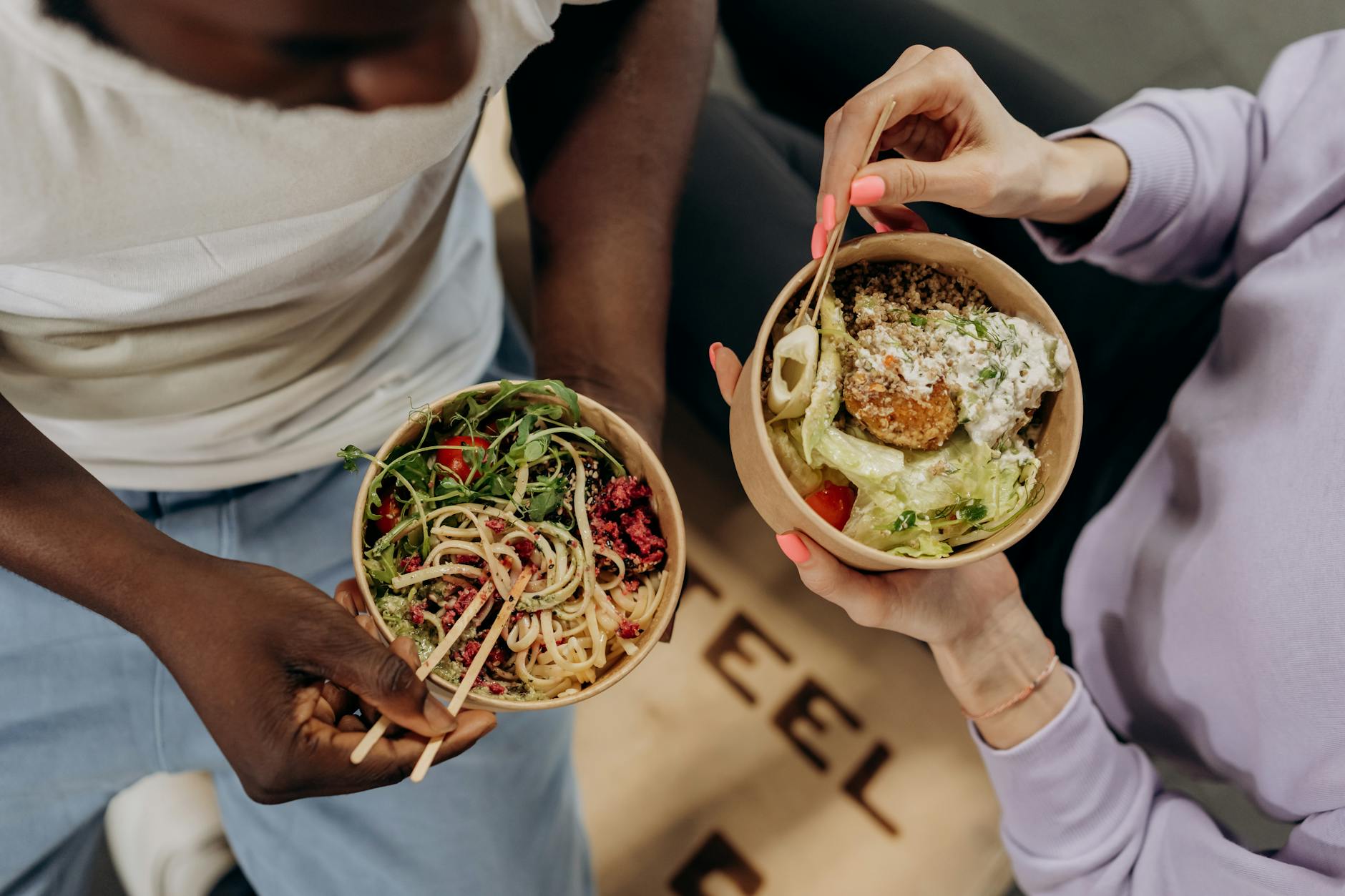 Two people holding bowls filled with salad and pasta, emphasizing healthy lifestyle choices. - mindful eating may