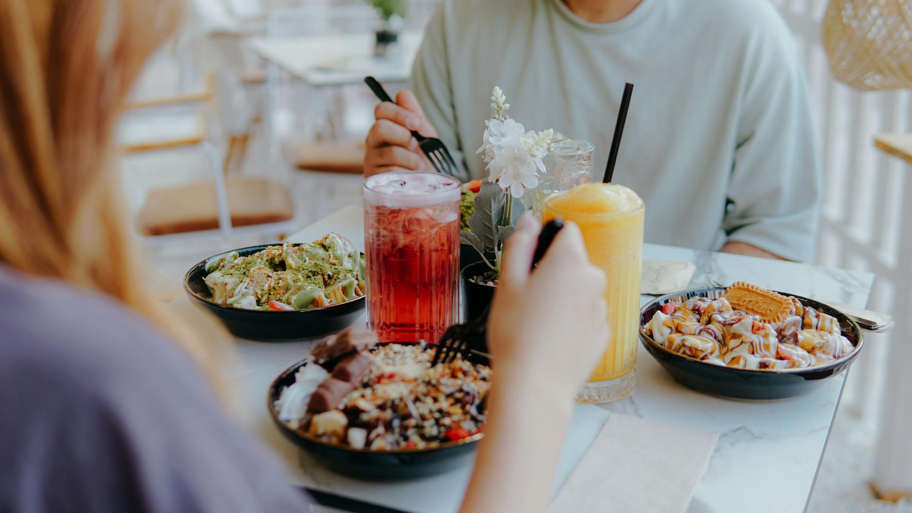 Two people enjoying a casual meal with various lunch bowls and refreshing drinks at a light-filled café. - mindful eating may