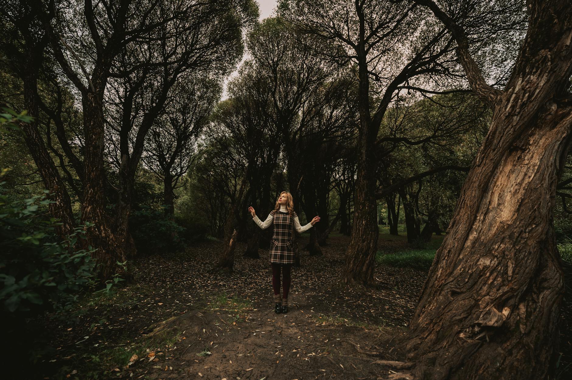 A woman in a plaid dress explores a serene autumn forest with towering trees. - mindful walking nature