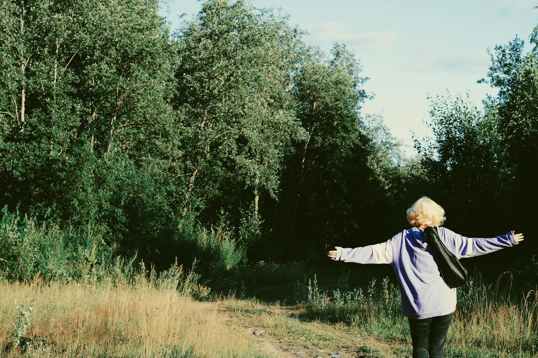 A woman with arms outstretched enjoys a peaceful walk in a forest setting, surrounded by trees and grass. - mindful walking nature