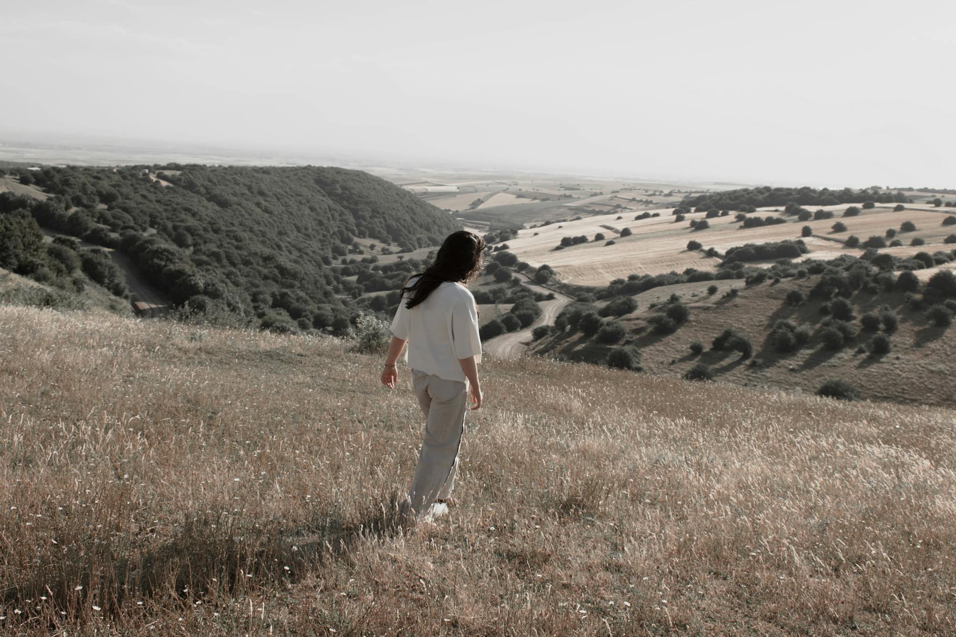 A woman walking peacefully on a hillside overlooking a serene valley and vast fields. - mindful walking nature