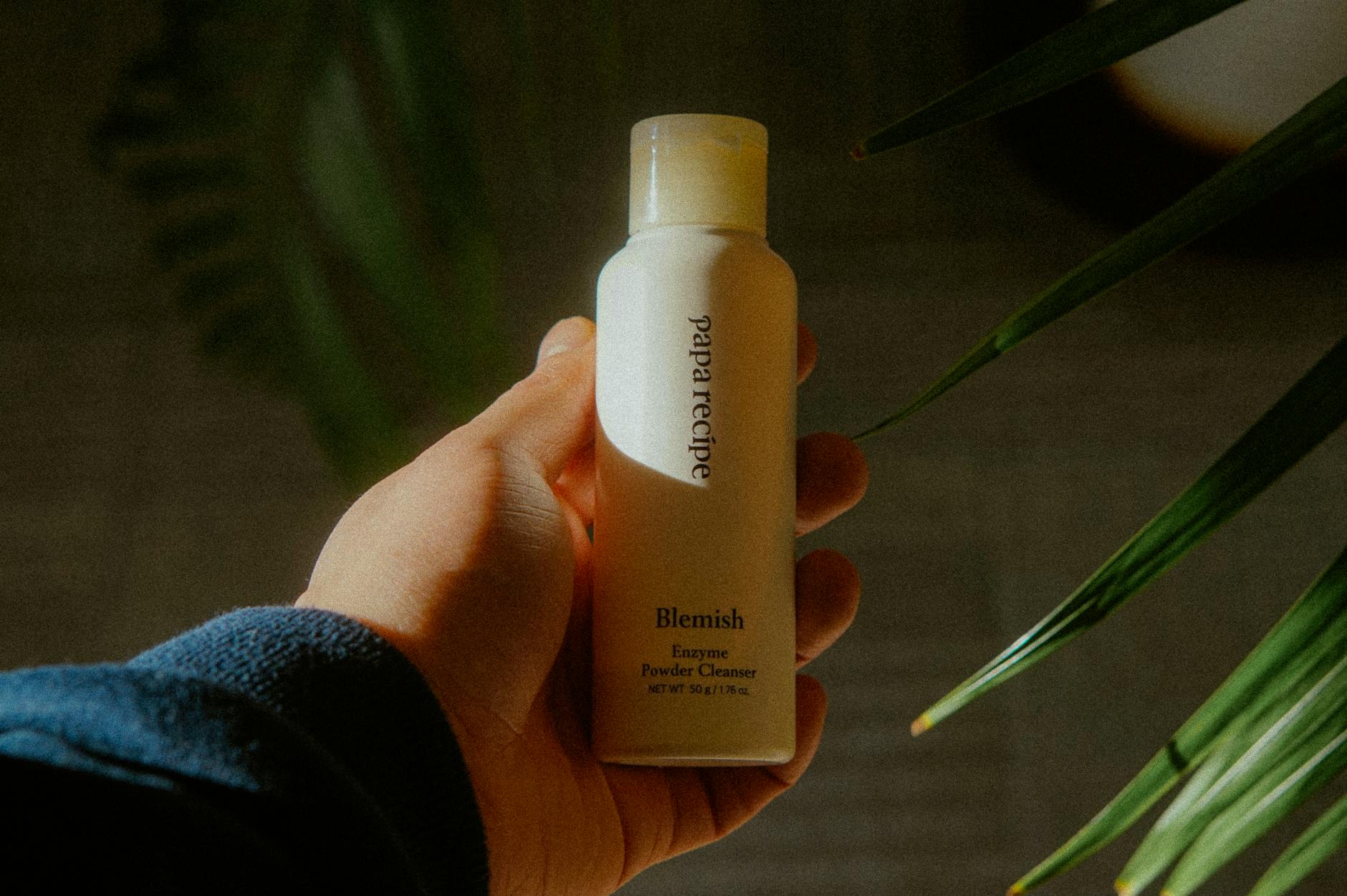 A close-up of a hand holding a Blemish Enzyme Powder Cleanser in natural light. - nourish skin from within