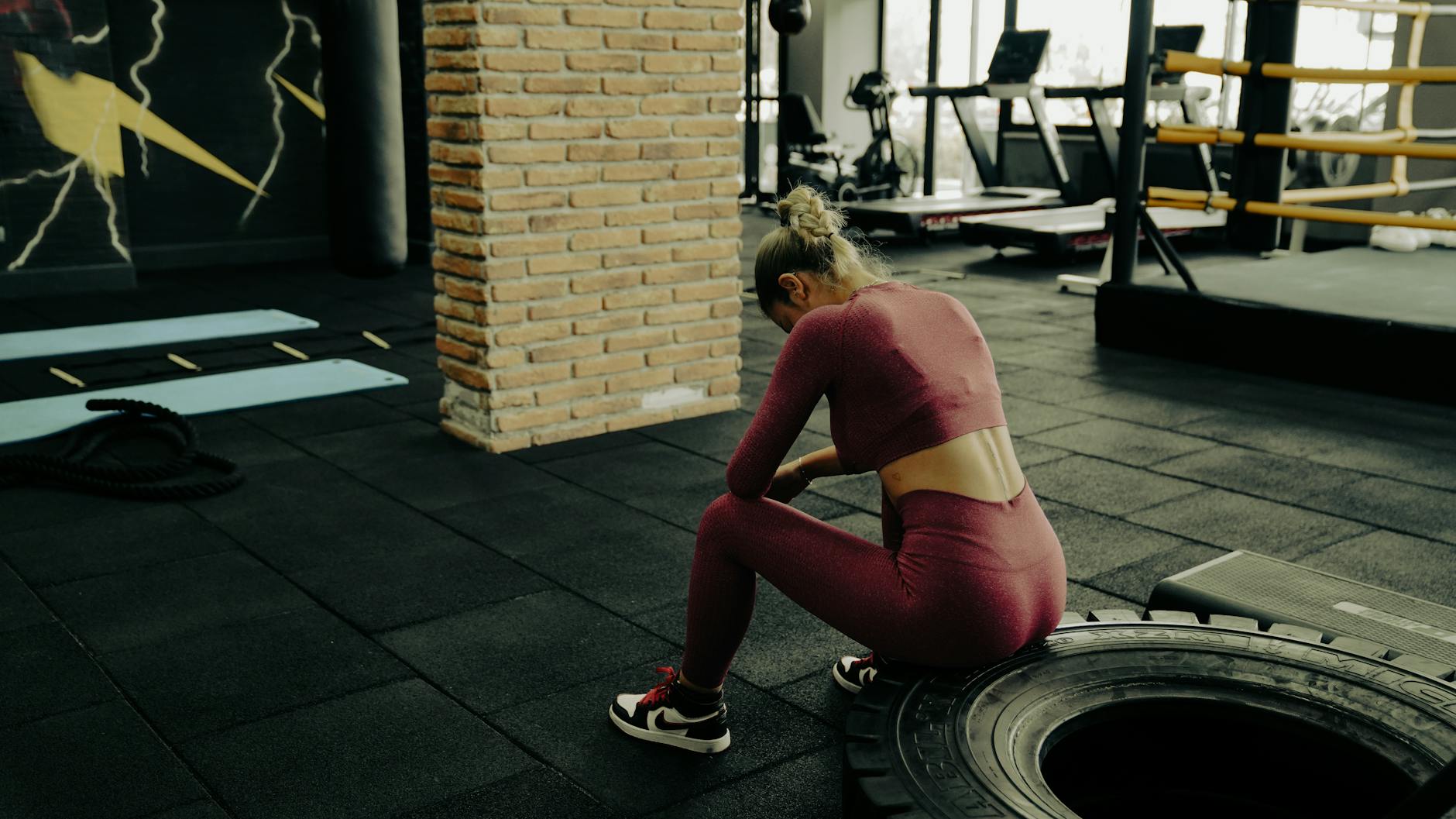 A woman in sportswear rests on a tire during gym training, showcasing fitness dedication. - nutrient timing fitness