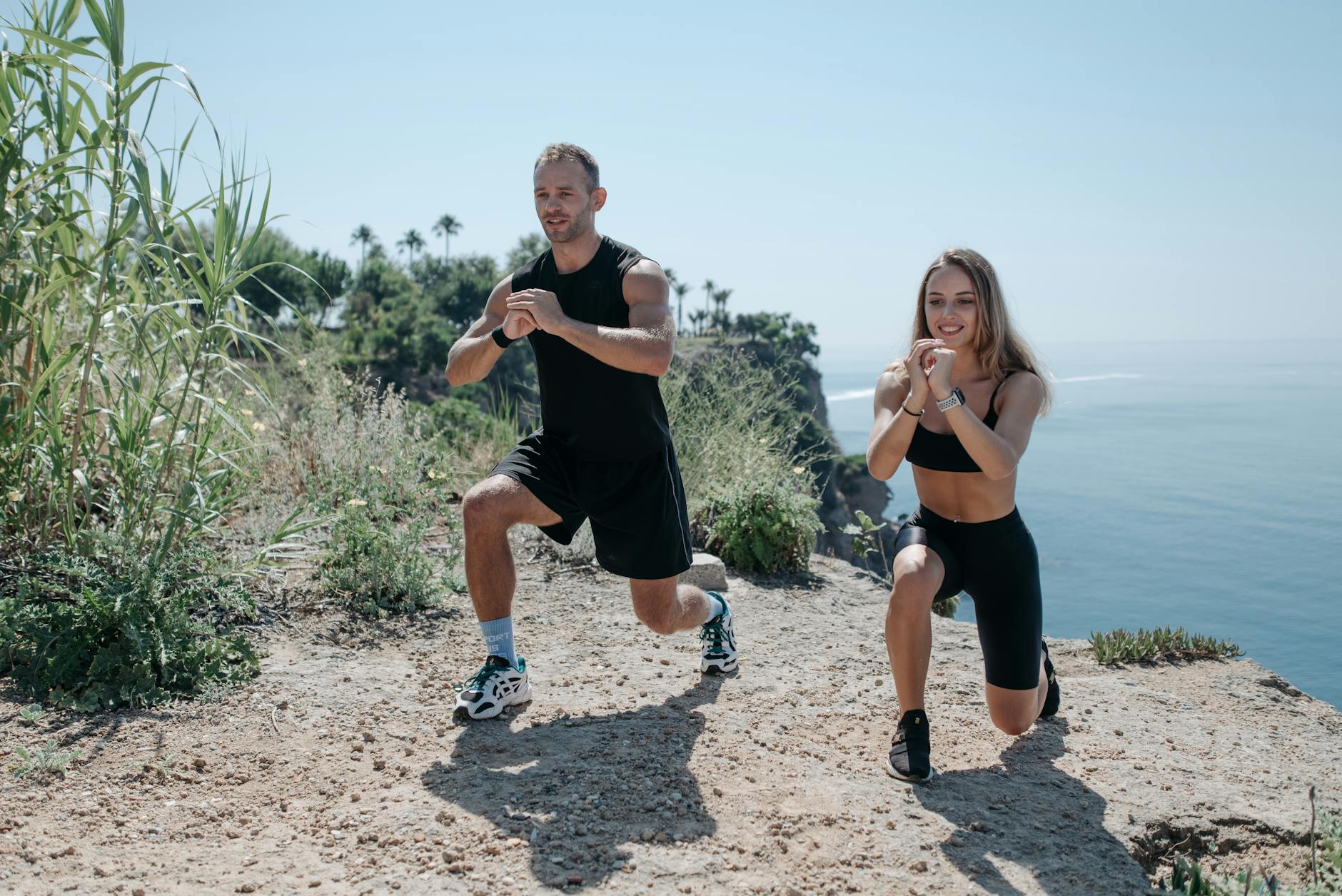 A man and woman exercising on a rocky cliff overlooking the ocean on a sunny day. - outdoor cardio workouts