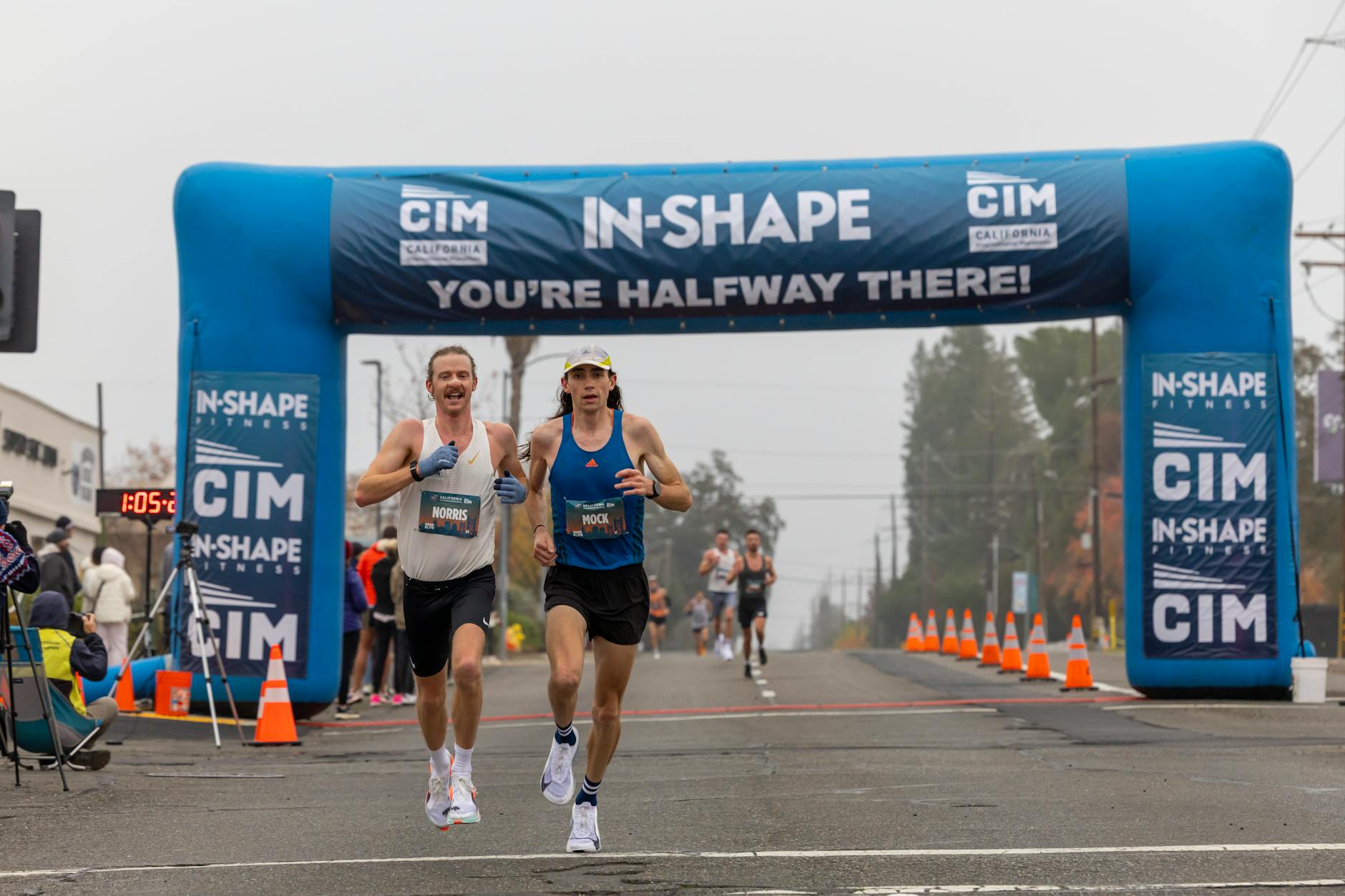 Two marathon runners competing in a foggy race reach the halfway mark under a blue archway. - outdoor running pace