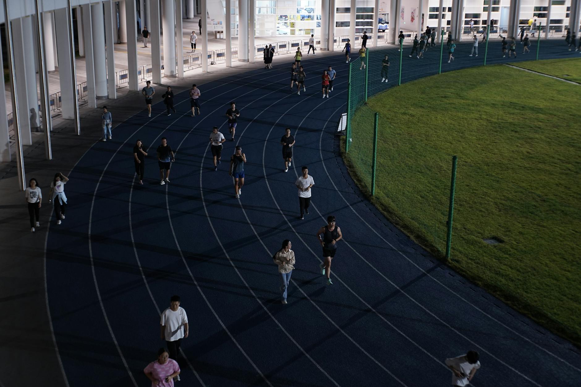 A group of people jogging on an outdoor track in the evening, showcasing urban fitness culture. - outdoor running pace
