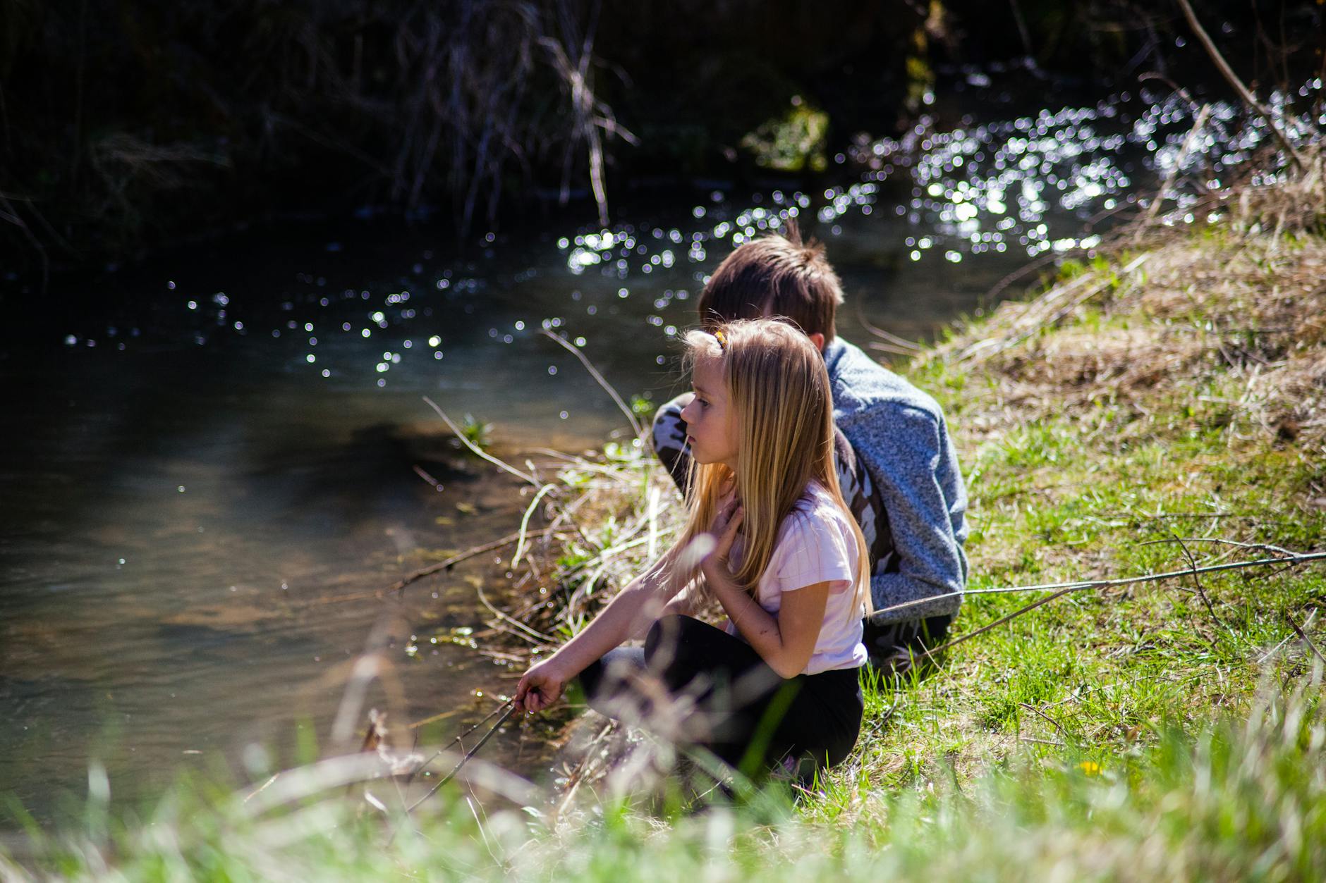 Two children enjoying a peaceful moment by a riverbank in spring. - outdoor spring activities