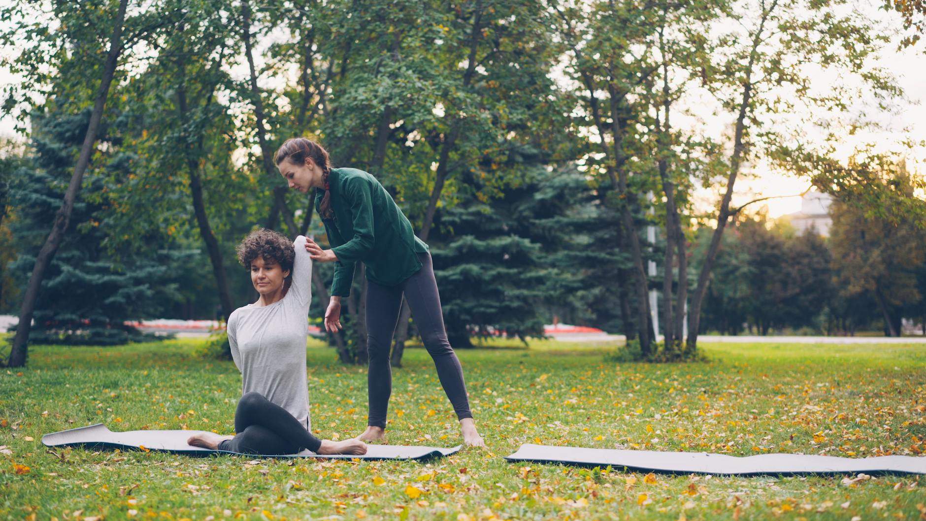 Two adult women practicing yoga in a park, with an instructor assisting one of them with a pose. - outdoor yoga beginner
