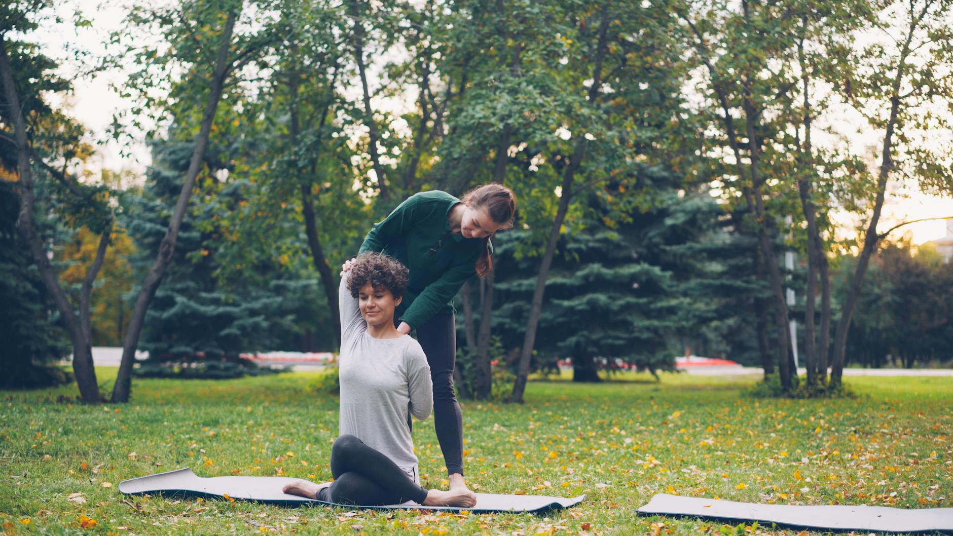 Woman practicing yoga outdoors with trainer's guidance in the park. - outdoor yoga beginner