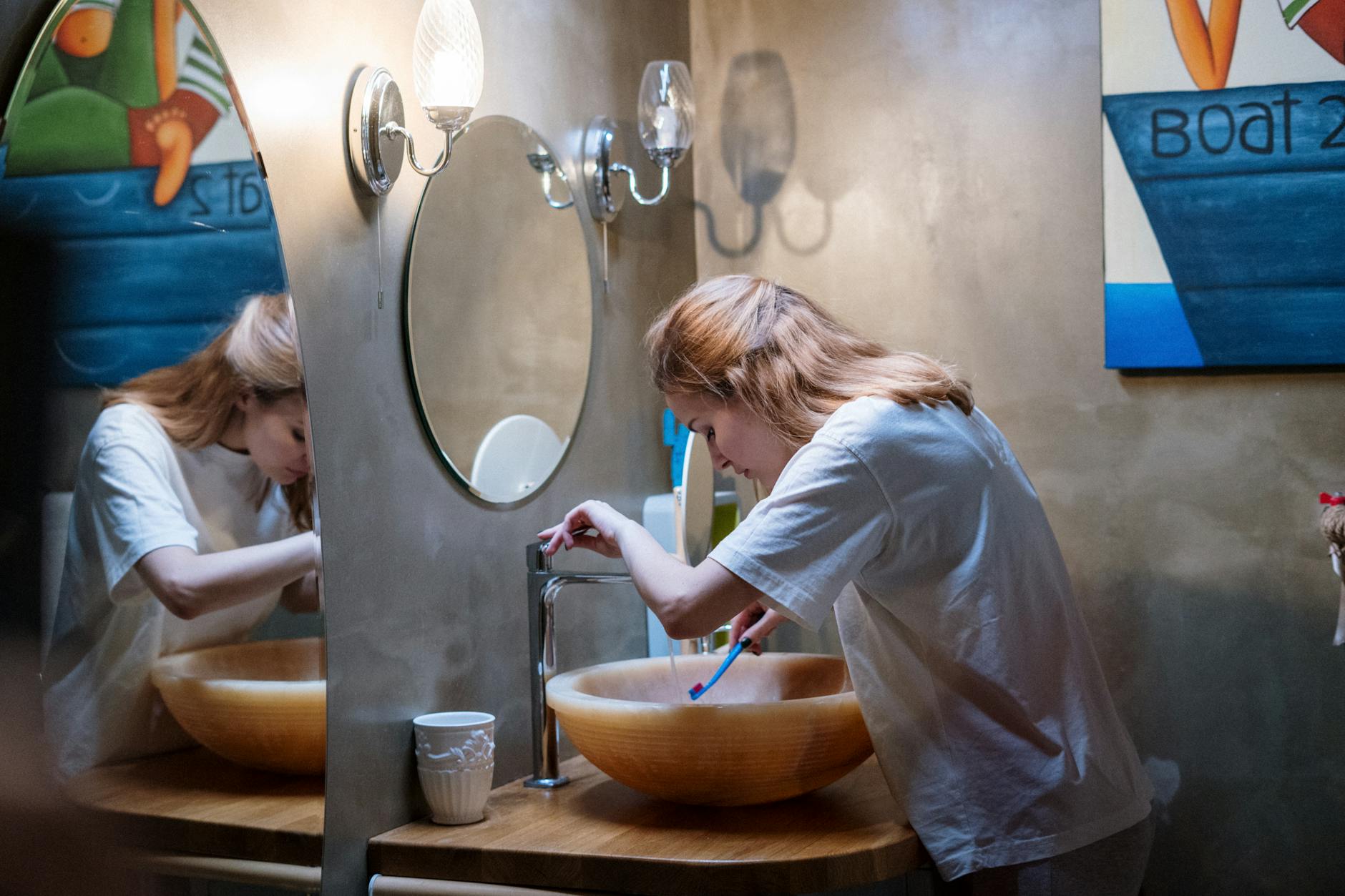 A woman brushing her teeth in a cozy, modern bathroom with warm lighting and artistic decor. - personal hygiene tips