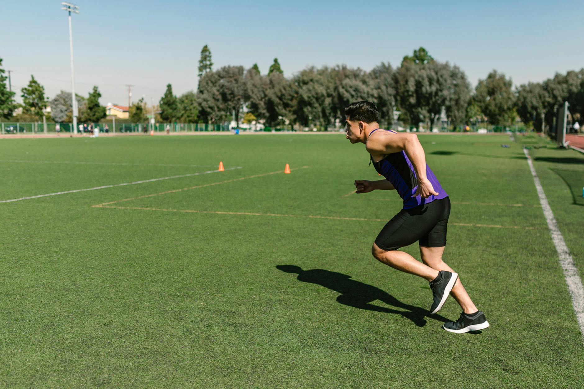 Asian male athlete runs during a workout on a grassy field wearing sportswear. - plyometric exercises