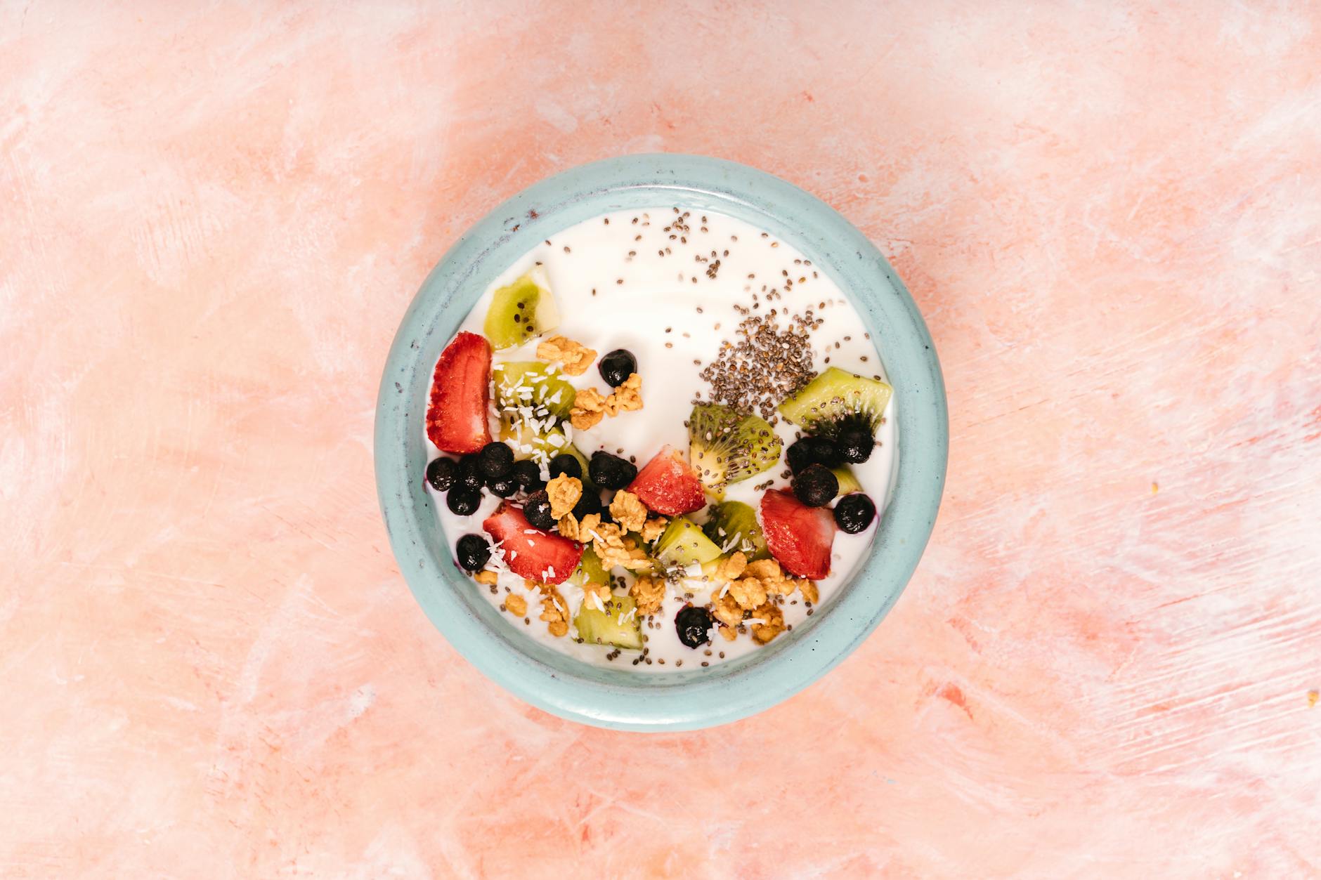 Top view of a nutritious breakfast bowl with yogurt, fresh fruits, and seeds on a pink background. - probiotics gut health