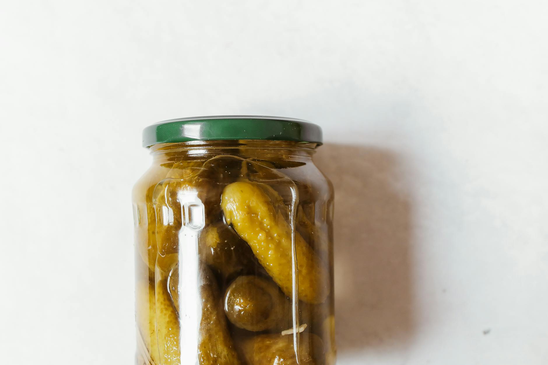 Close-up of a glass jar filled with pickles on a white surface. - probiotics gut health