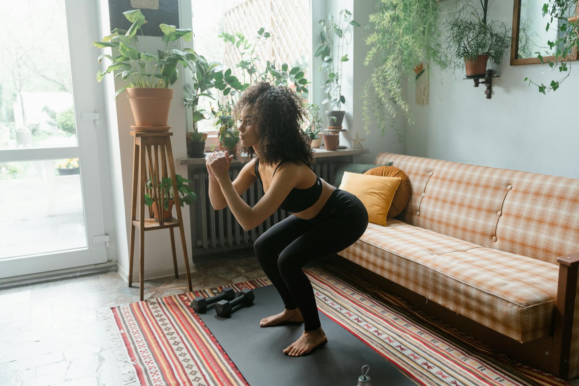 Woman in active wear doing squats on a yoga mat in a cozy indoor setting with plants and natural light. - quick at home workouts