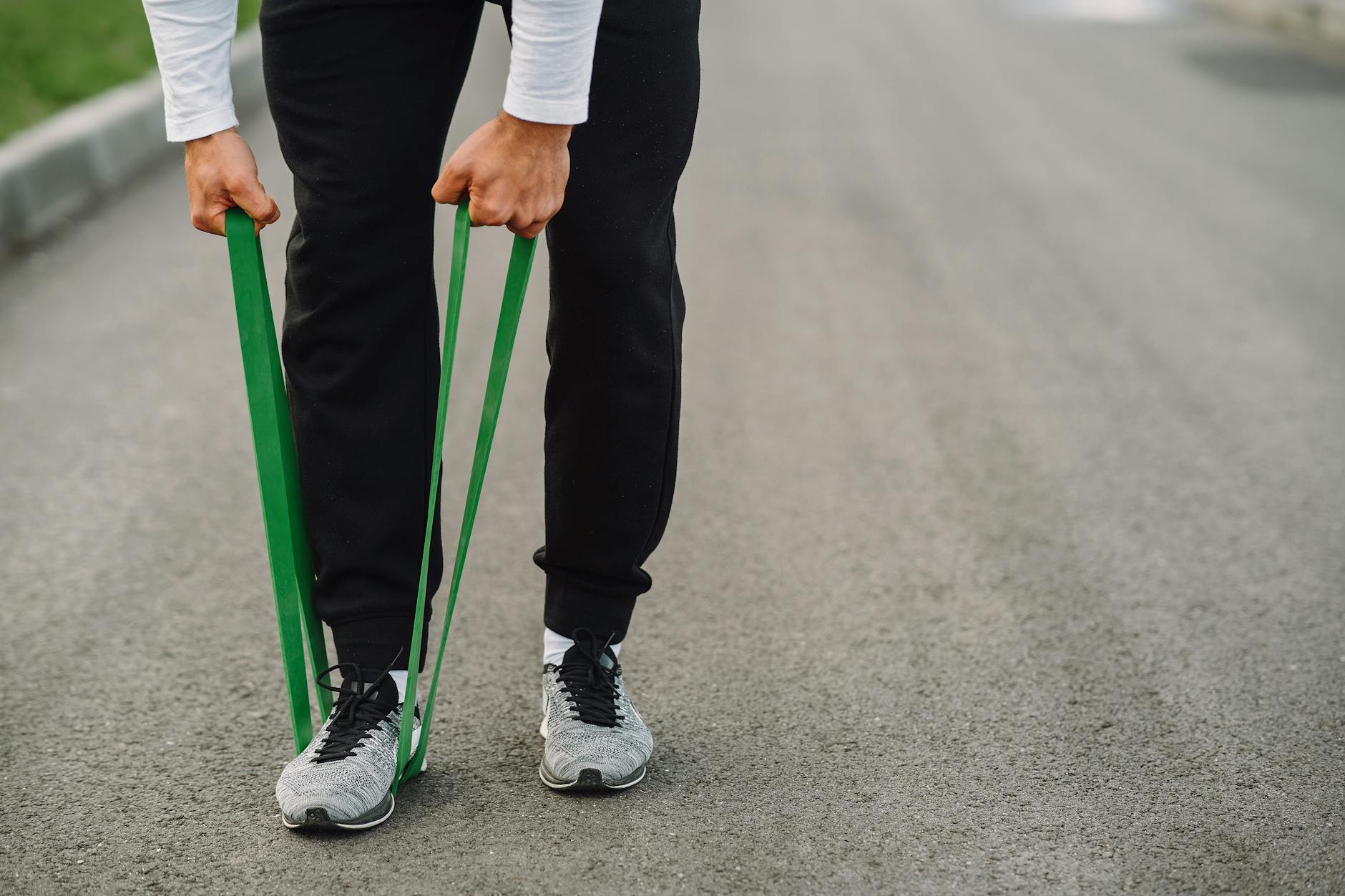 An athlete uses green resistance bands for a workout on a paved path. - resistance band abs