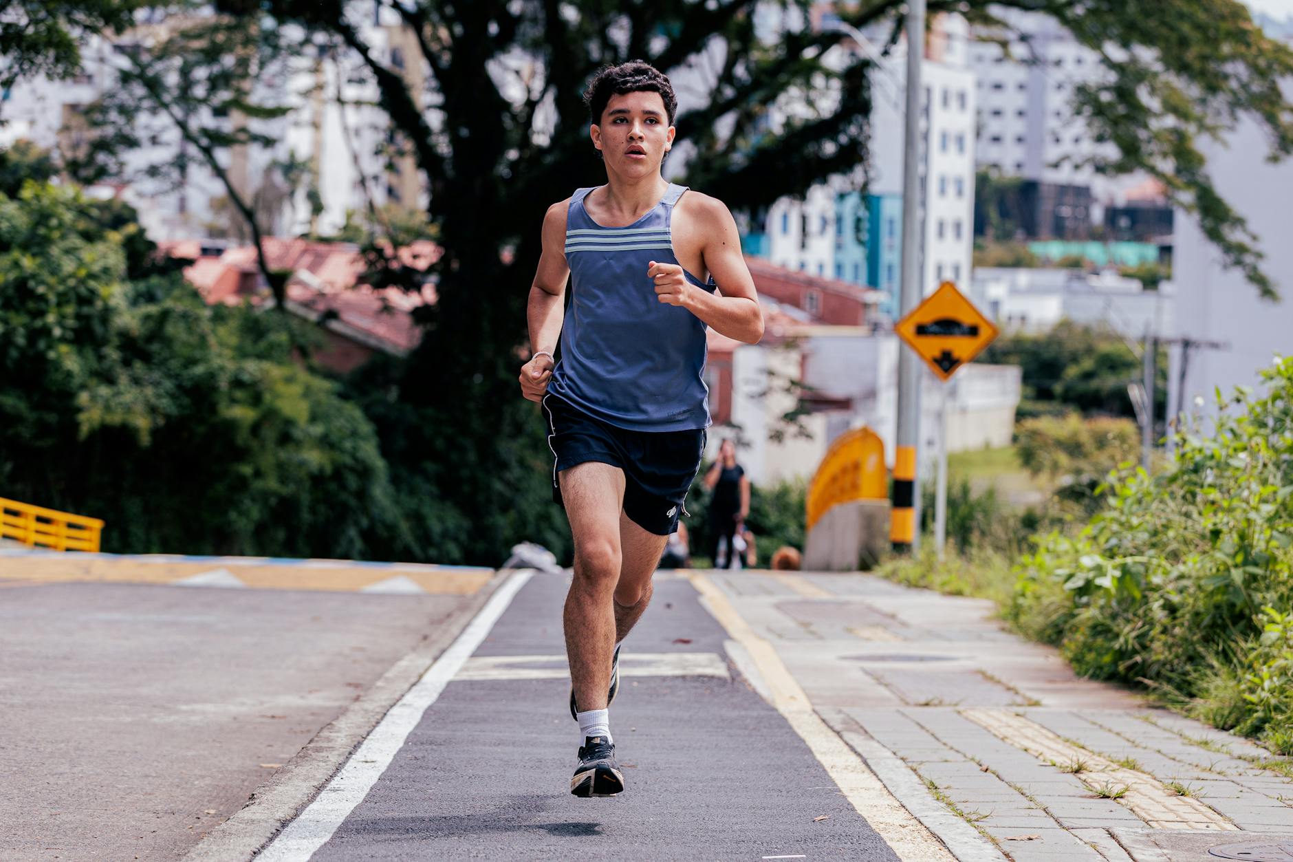 Energetic young man jogging outdoors on a city street surrounded by greenery on a sunny day. - running tips for beginners