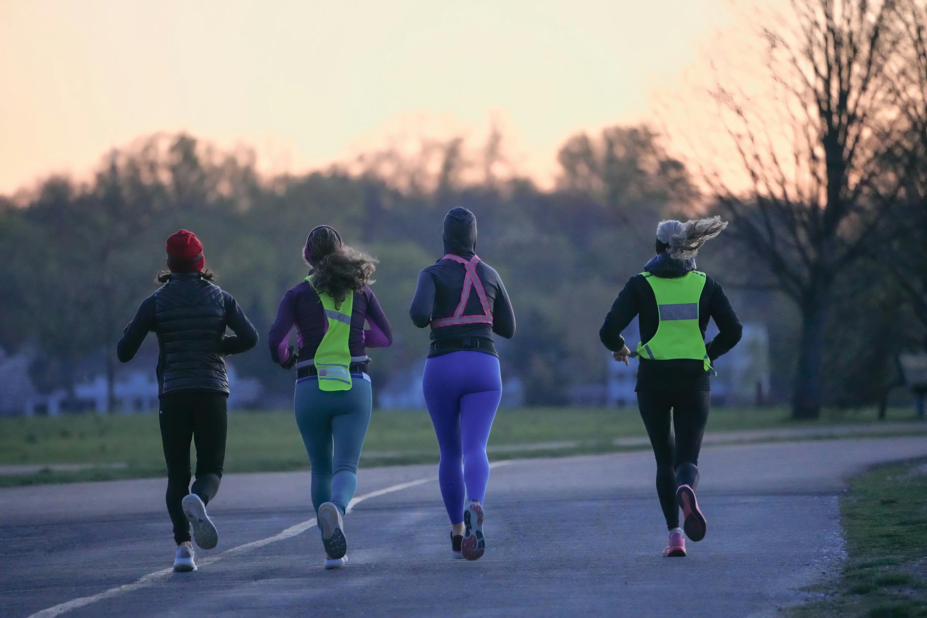Four people running outdoors at dawn, wearing activewear and reflective gear for visibility. - running tips for beginners