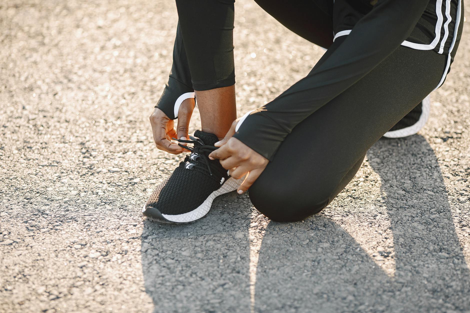 Close-up of a person tying black sports shoes on a sunny day, outdoors. - running tips for beginners
