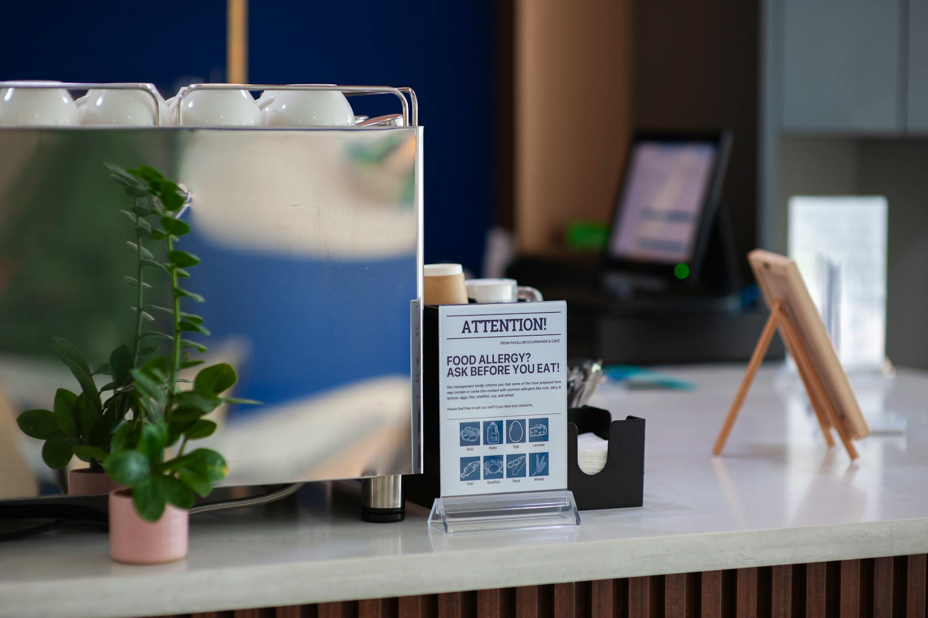 Coffee shop counter featuring an allergy warning sign and plant, highlighting food safety. - spring allergy triggers