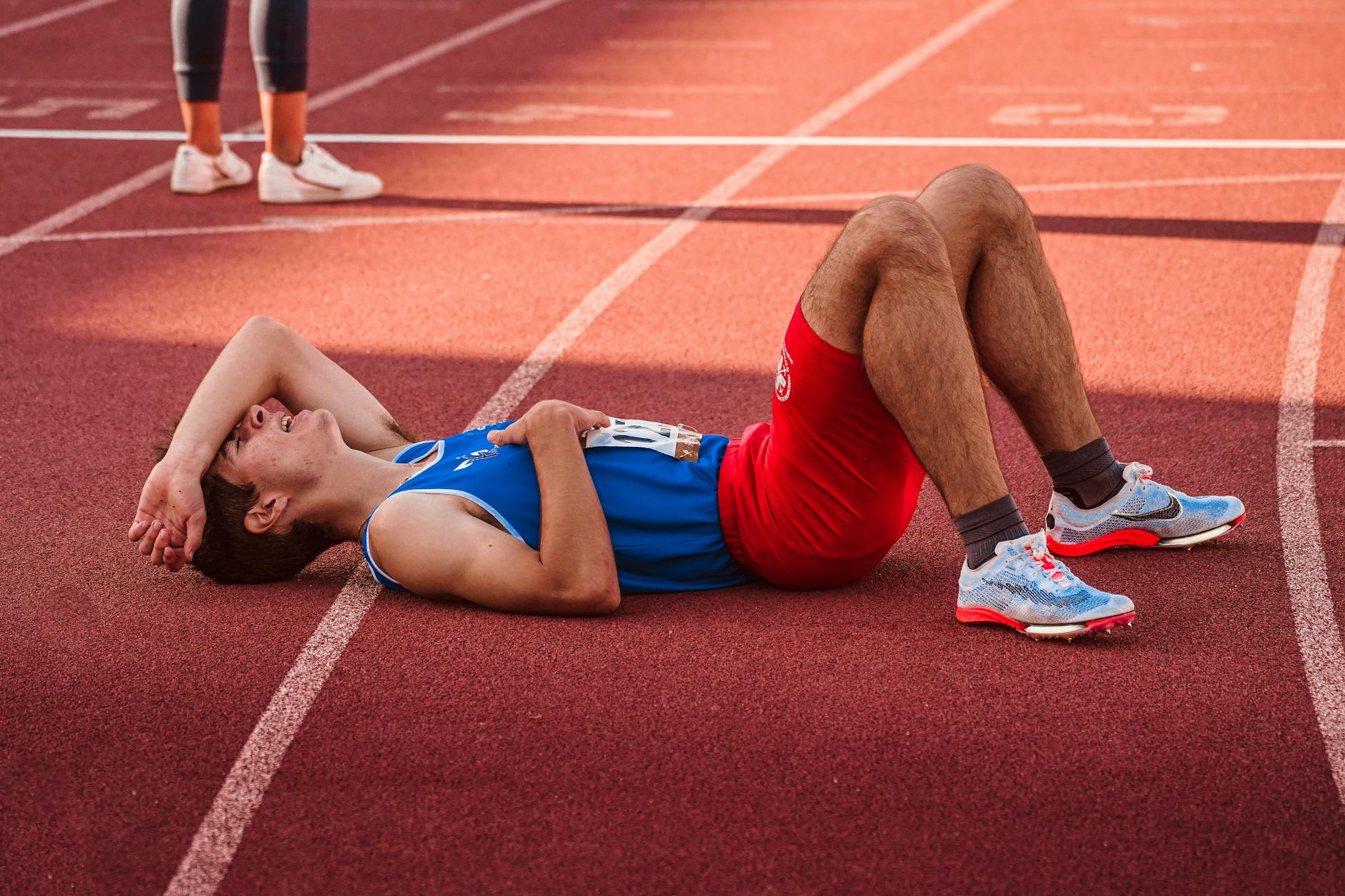 A tired athlete lies on the track, recovering after a race in sportswear. - spring athlete recovery