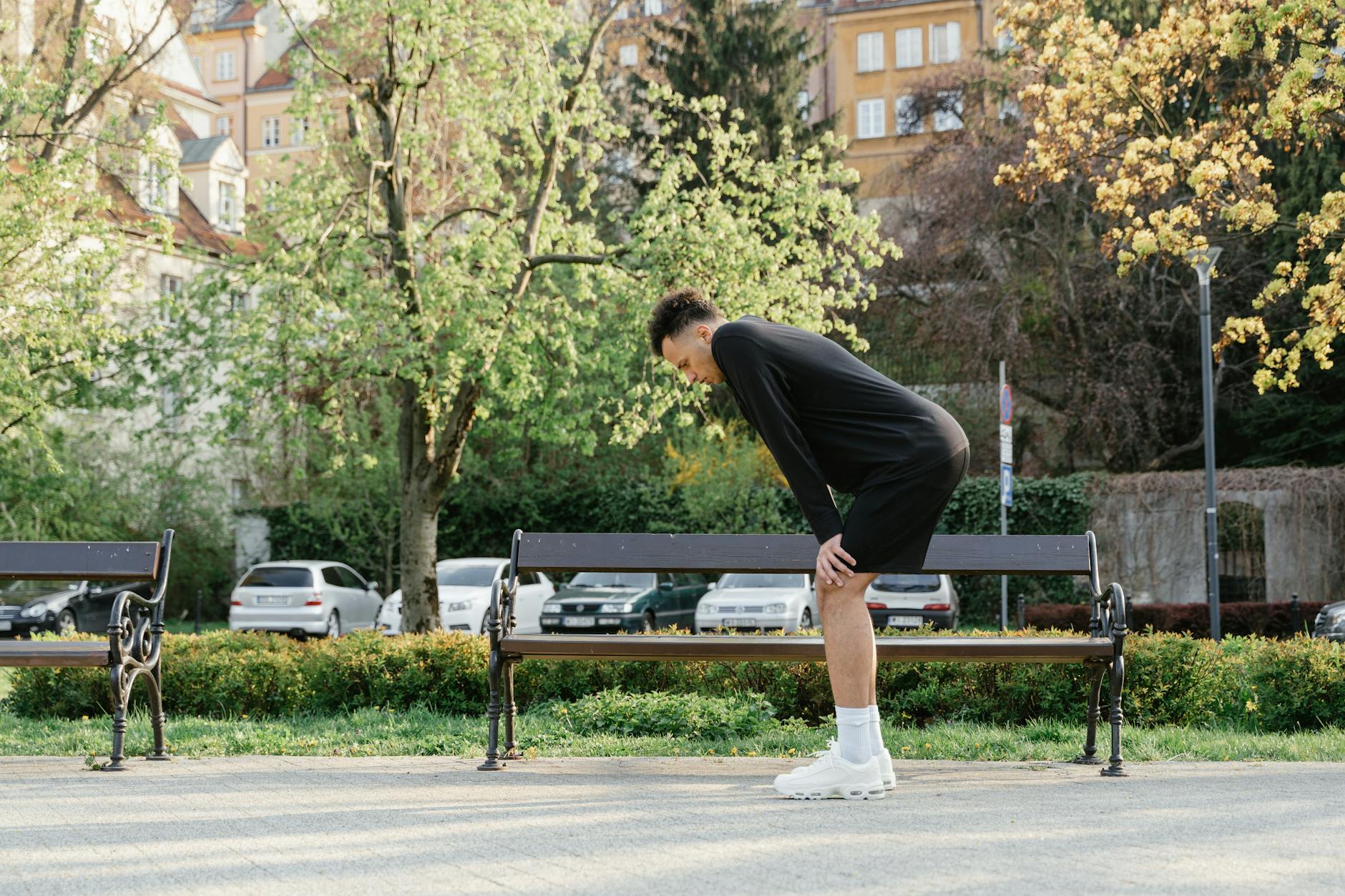 An athletic man bends forward to catch his breath in a sunny outdoor park. - spring athlete recovery