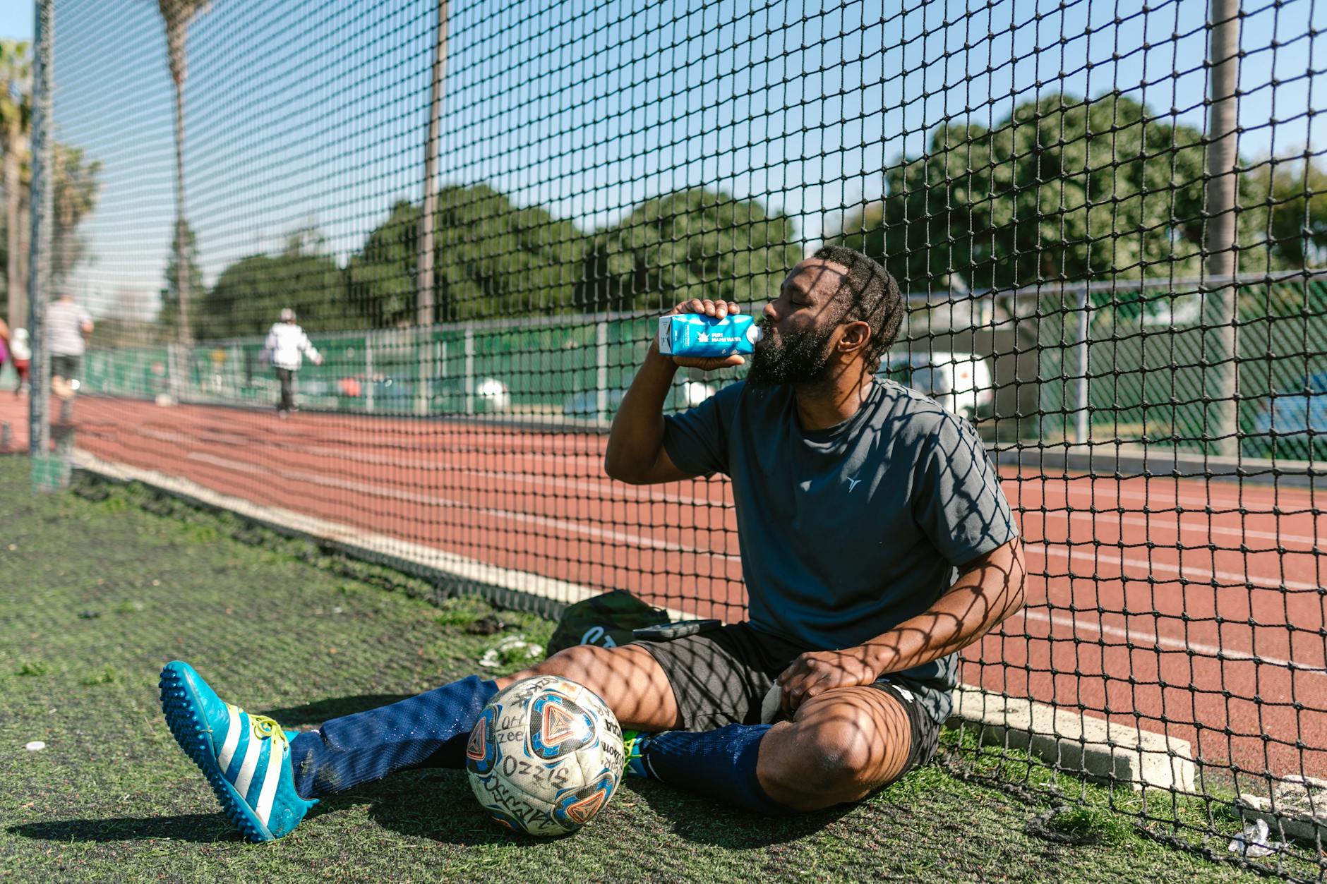 Soccer player resting by a field, hydrating after practice on a sunny day. - spring athlete recovery
