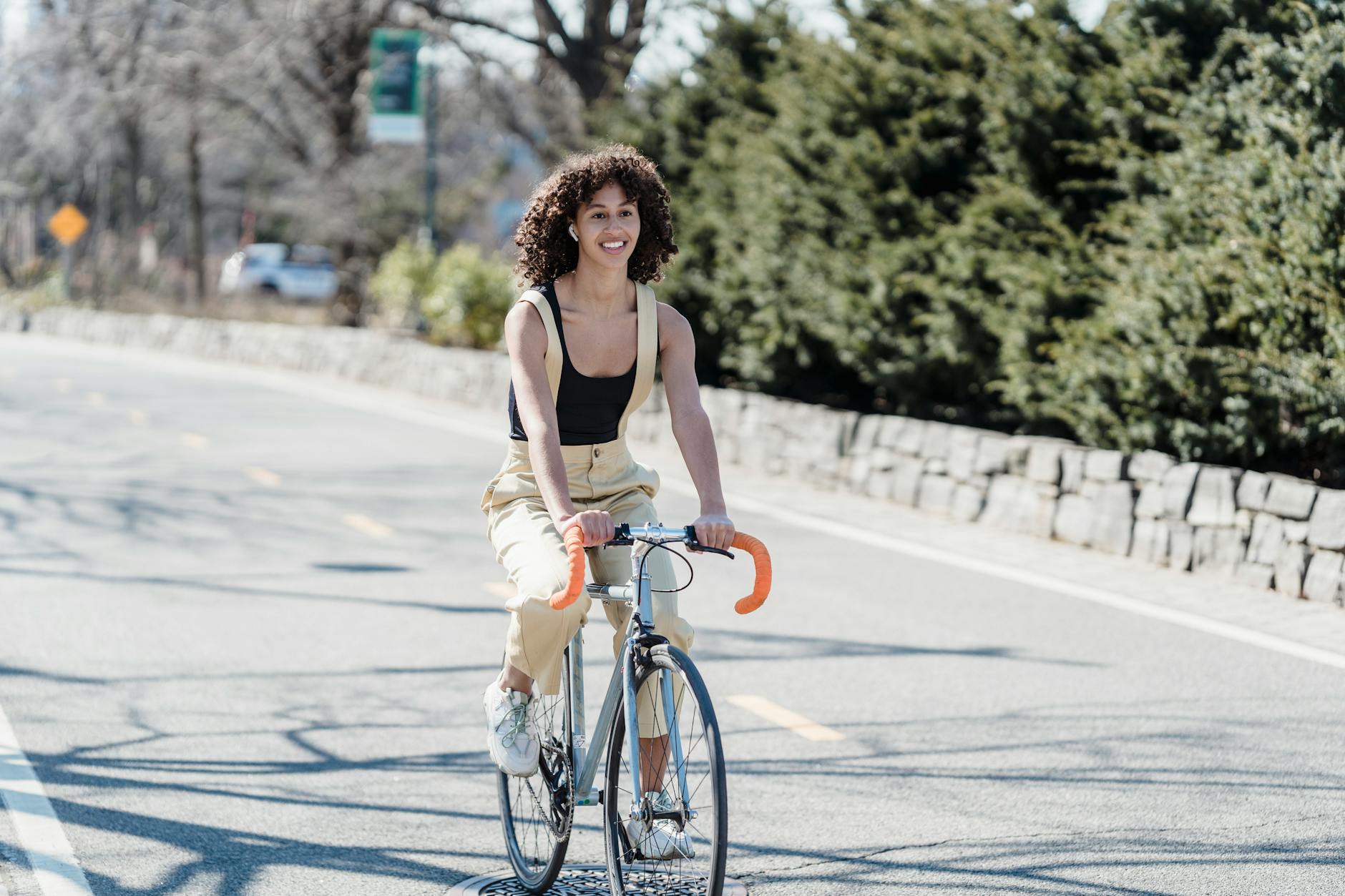 Young woman with curly hair riding a road bike on a sunny day, enjoying leisure time outdoors. - spring cycling fitness